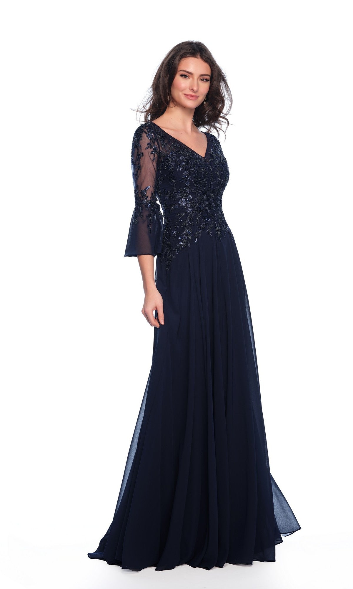 A woman models the Long Formal Dress 11602 by Dave and Johnny—floor-length, navy blue with a v-neckline, lace and sequin bodice, and sheer three-quarter sleeves—standing against a white background.