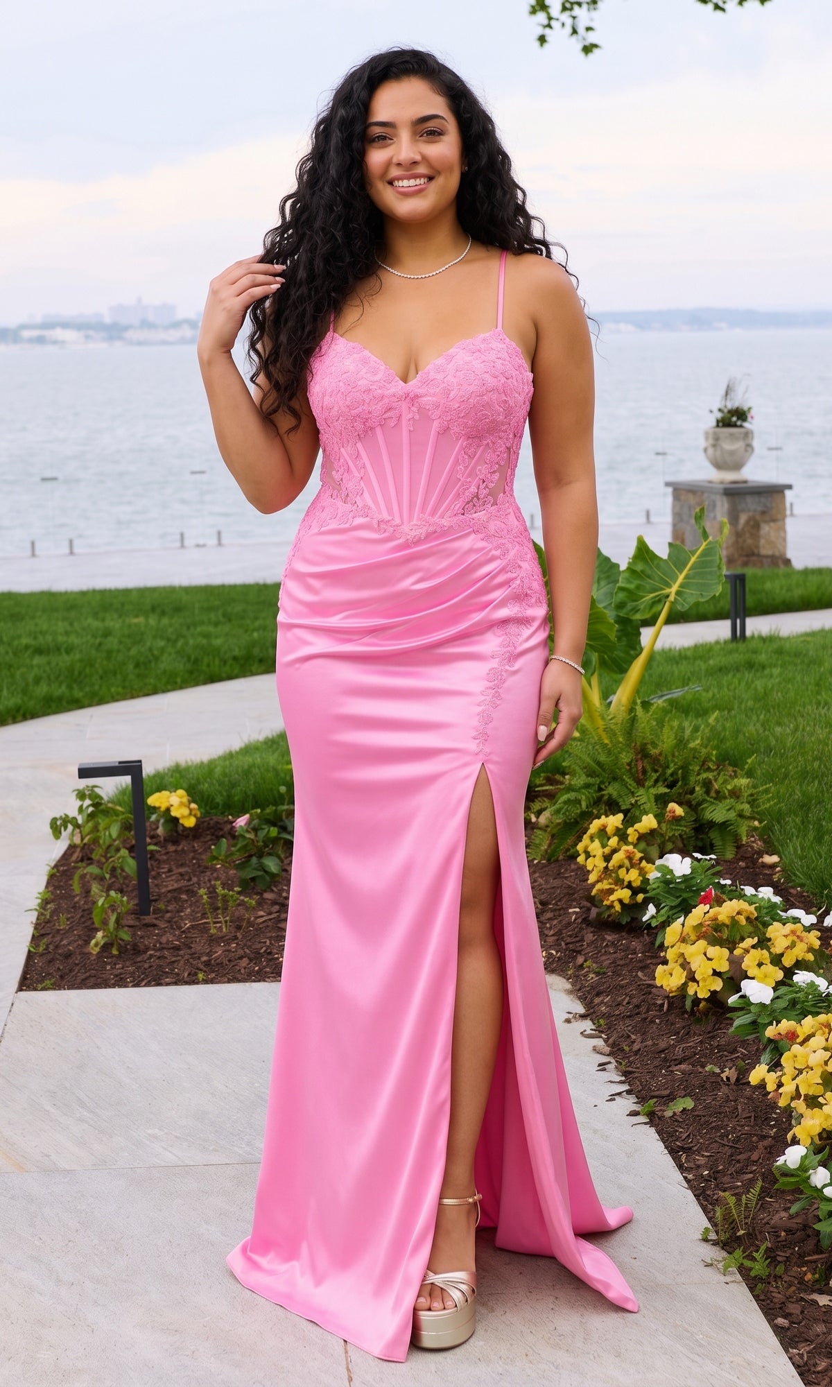 A person wears a cotton candy pink Long Plus-Size Prom Dress: Faviana 11605E, featuring a floor-length skirt with a high thigh slit and a lace-appliqued corset bodice.