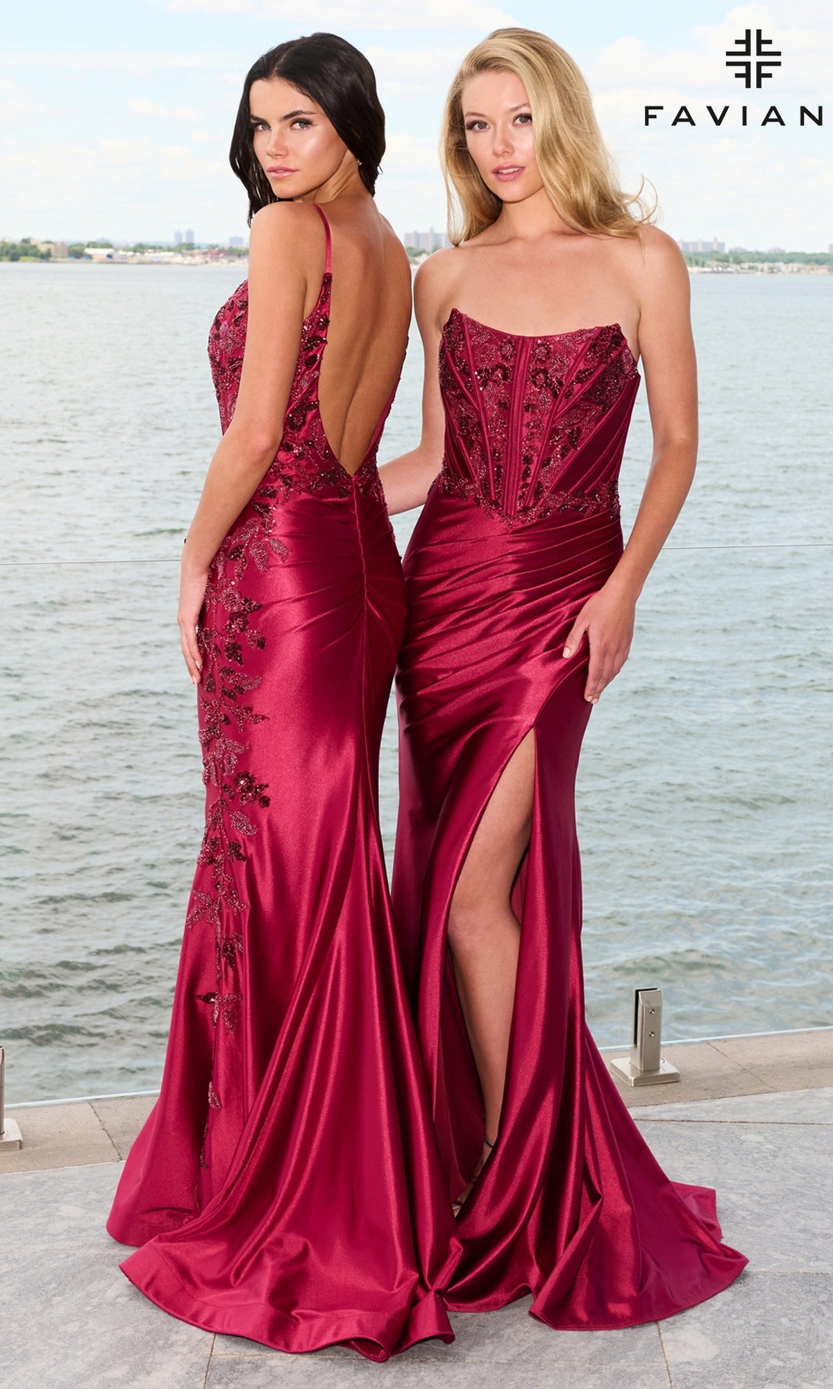 Two women stand by a waterfront wearing floor-length, deep red Faviana 11609 satin gowns with intricate beaded leaf appliques on the bodices.