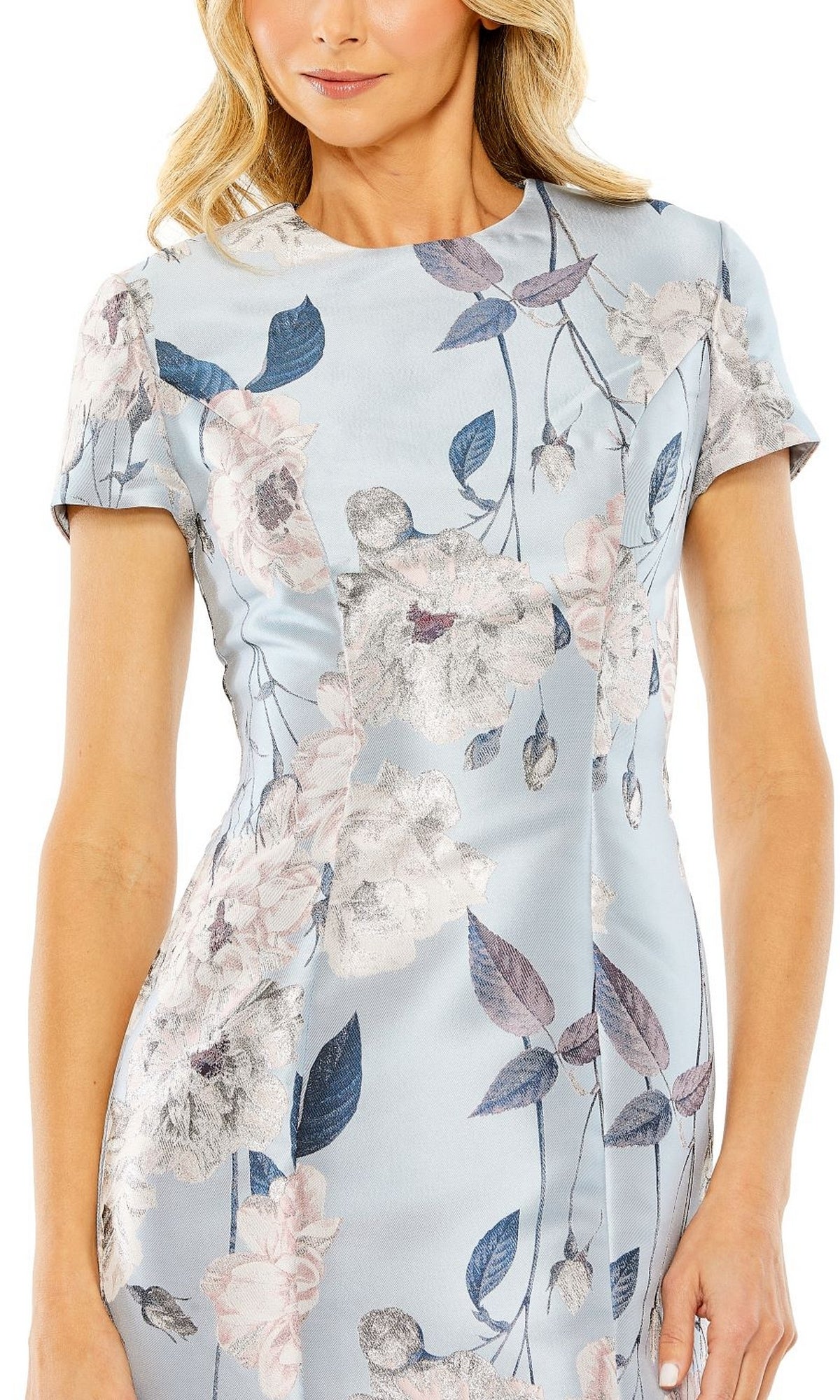 A woman wearing the Mac Duggal Floral-Print Wedding-Guest Dress 11614, a light blue short-sleeve dress decorated with large pale flowers and dark leaves.