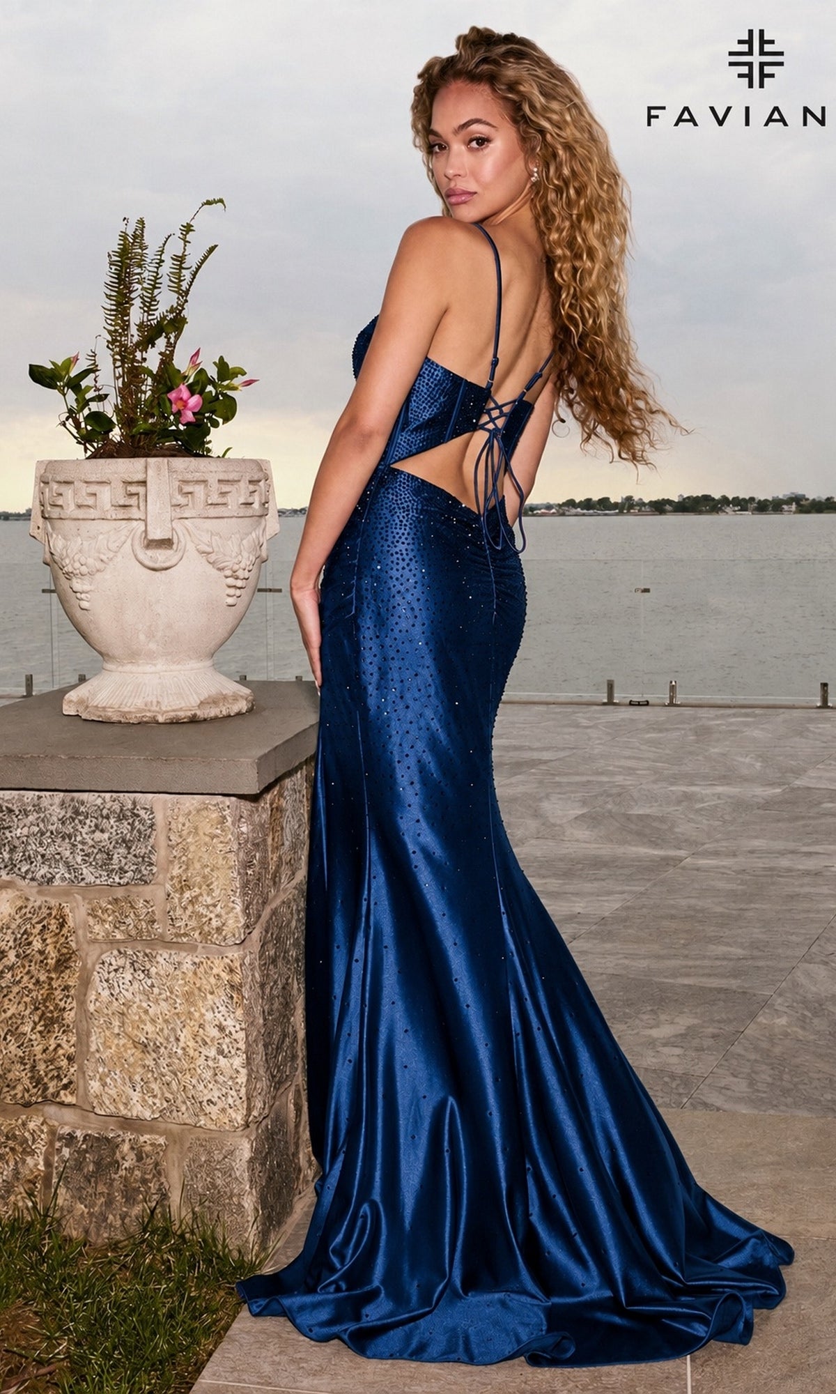 A person wearing a navy Long Prom Dress: Faviana 11621 mermaid-style gown with a plunging V-neckline, lace-up open back, and scattered rhinestone embellishments.