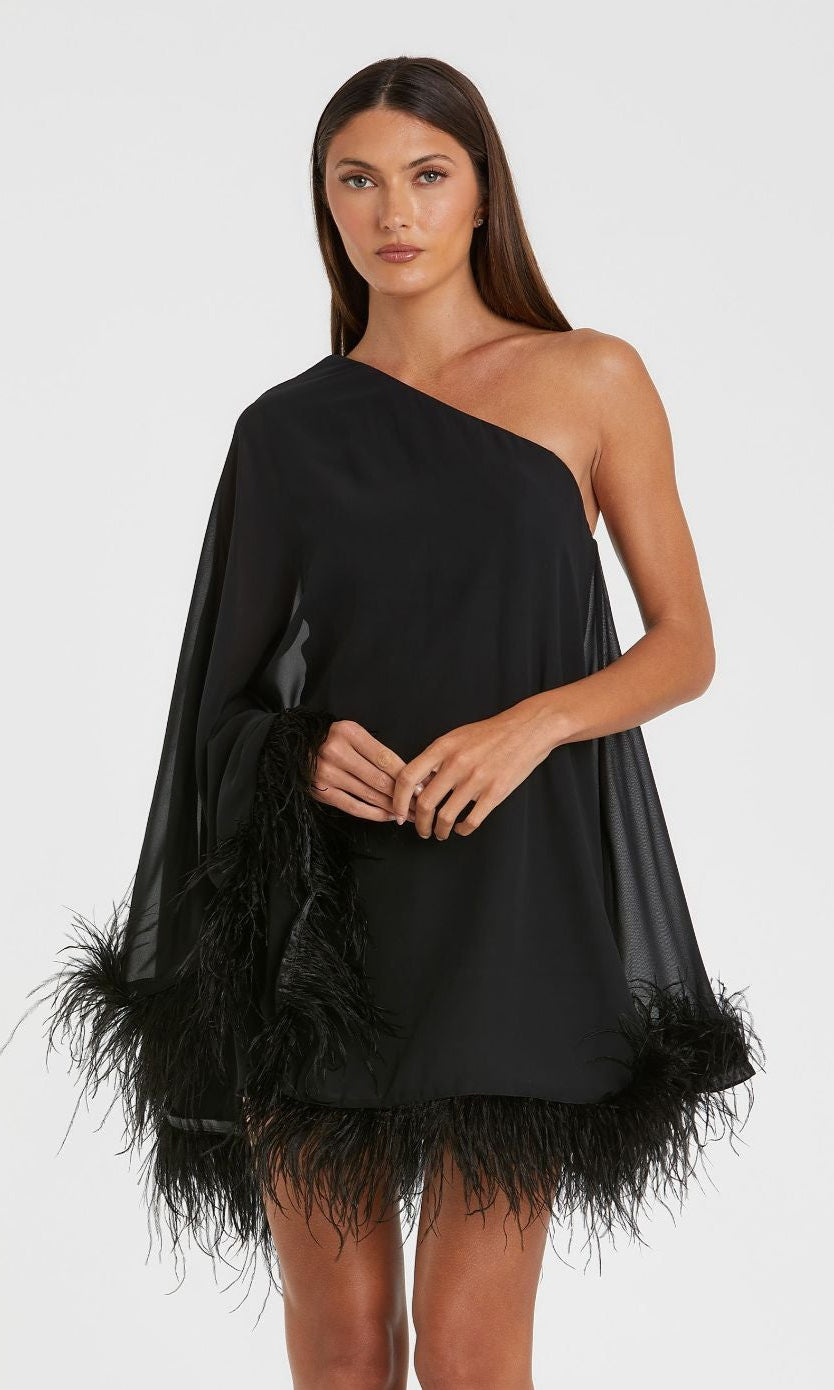 A woman stands against a white background wearing the Mac Duggal 11623 short wedding guest dress, featuring a black one-shoulder design with feather-trimmed hem and sleeve.