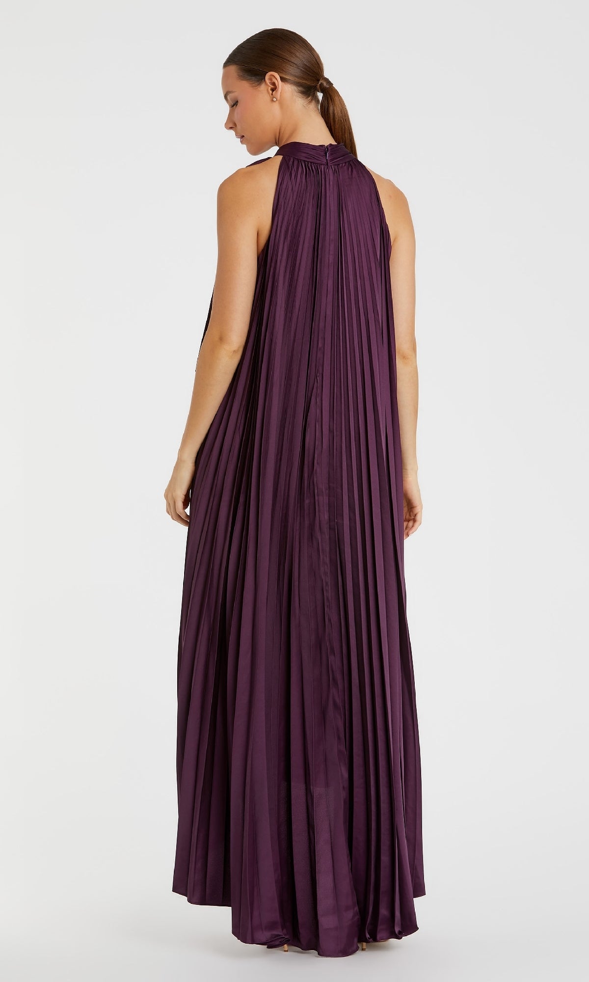 A woman stands with her back to the camera against a white background, wearing the Mac Duggal 11639 Long Plum Purple Formal Dress—a sleeveless, floor-length gown with elegant pleats.