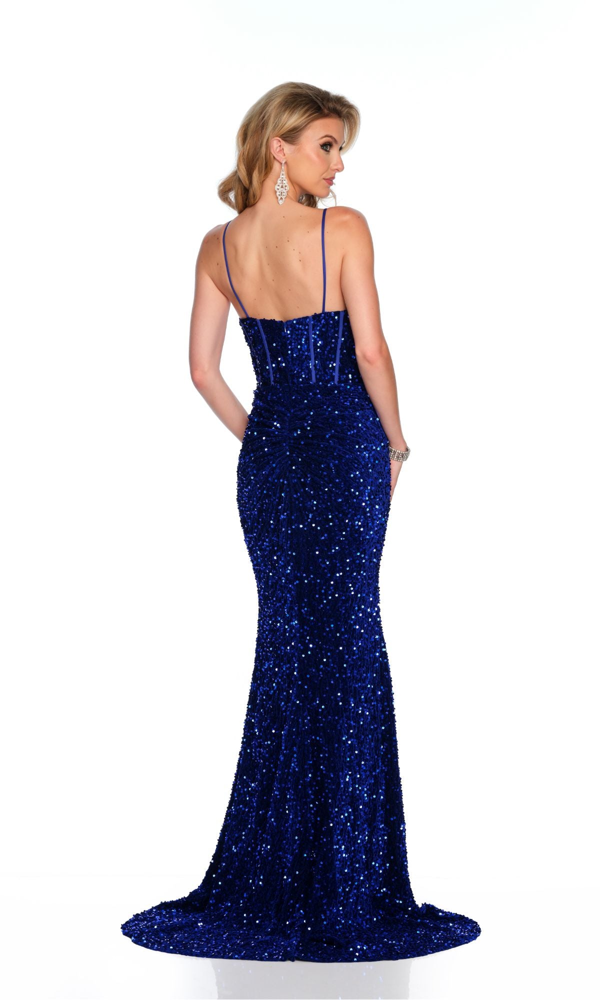 A woman models the Long Formal Dress 11652 by Dave and Johnny—an elegant fitted royal blue sequin gown with thin straps—standing against a white background to showcase the stunning back design.