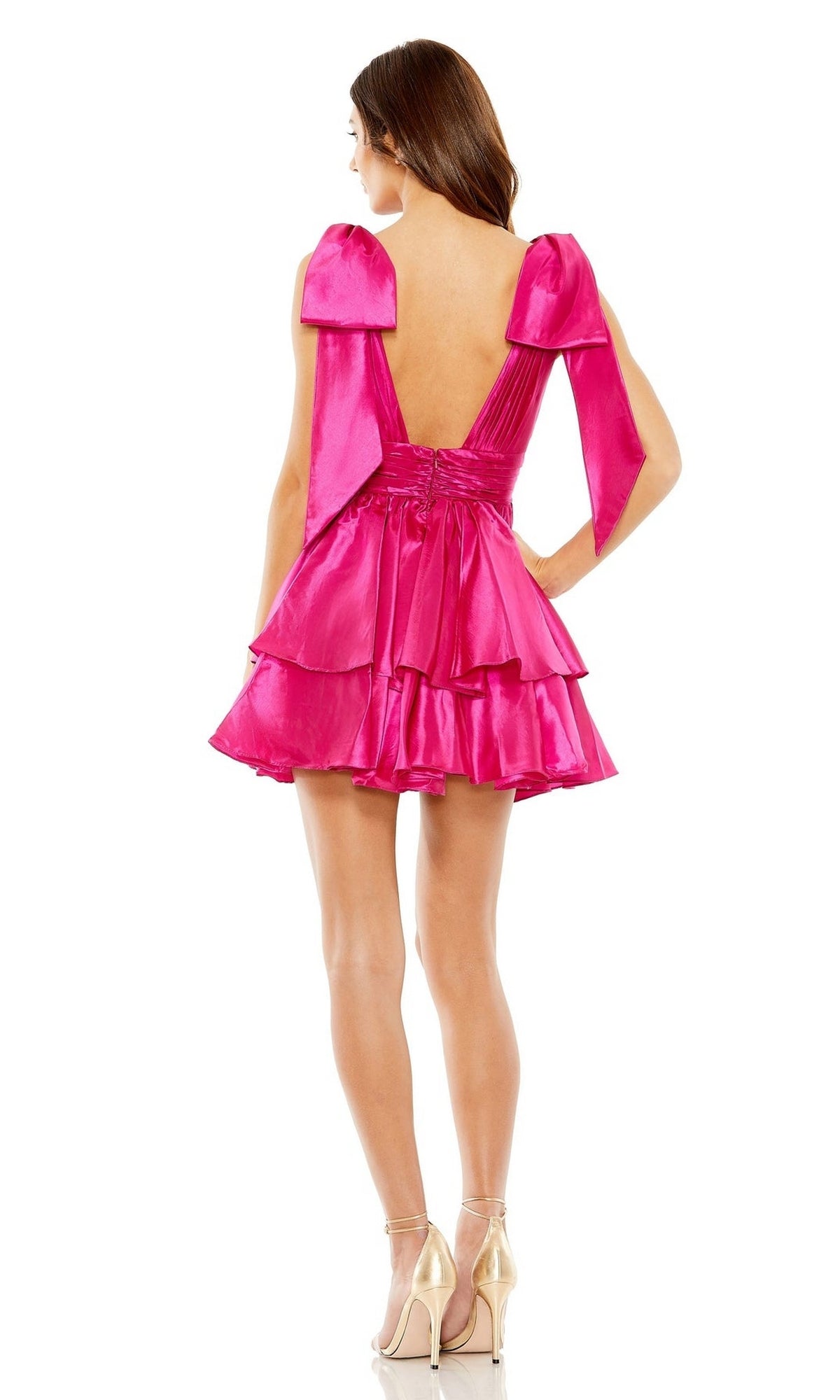 Woman wearing the Mac Duggal 11657 Bow Short Ruffled Hoco Dress in bright pink, with shoulder bows and open-back design, stands in heels facing away from the camera.