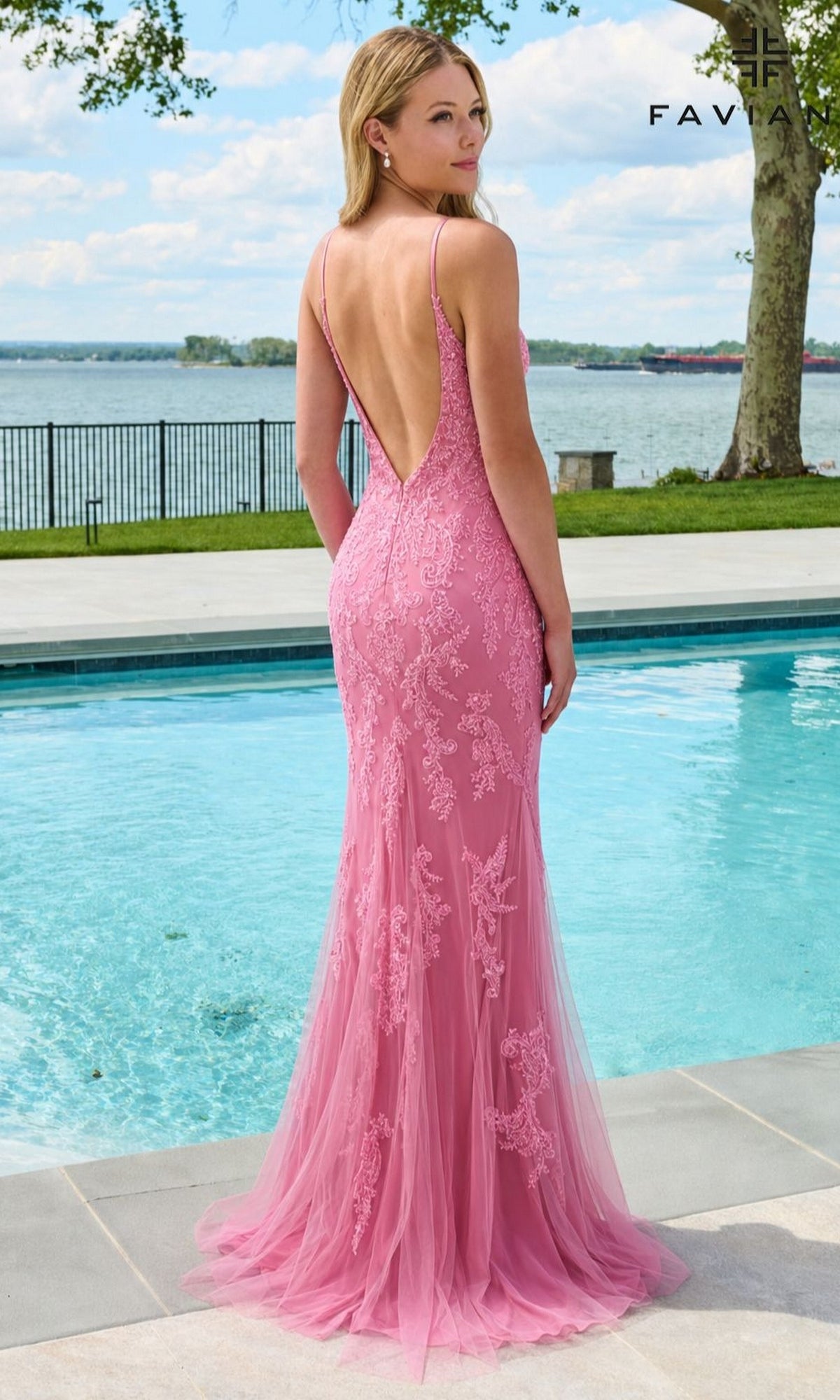 A woman stands by a swimming pool wearing a floor-length, backless pink Faviana 11678 gown featuring delicate beaded lace appliques.