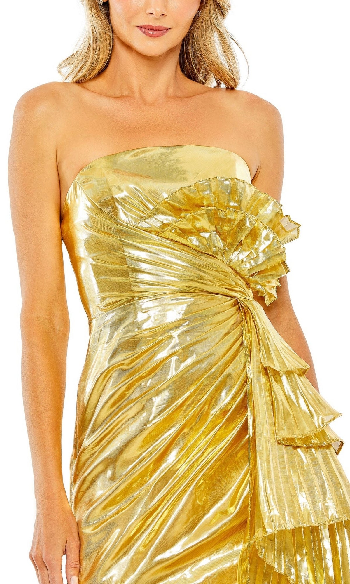 A woman wears the Mac Duggal Short Homecoming Dress 11695, a strapless metallic gold party dress with pleated detailing, a pleated side sash, and front ruffles.