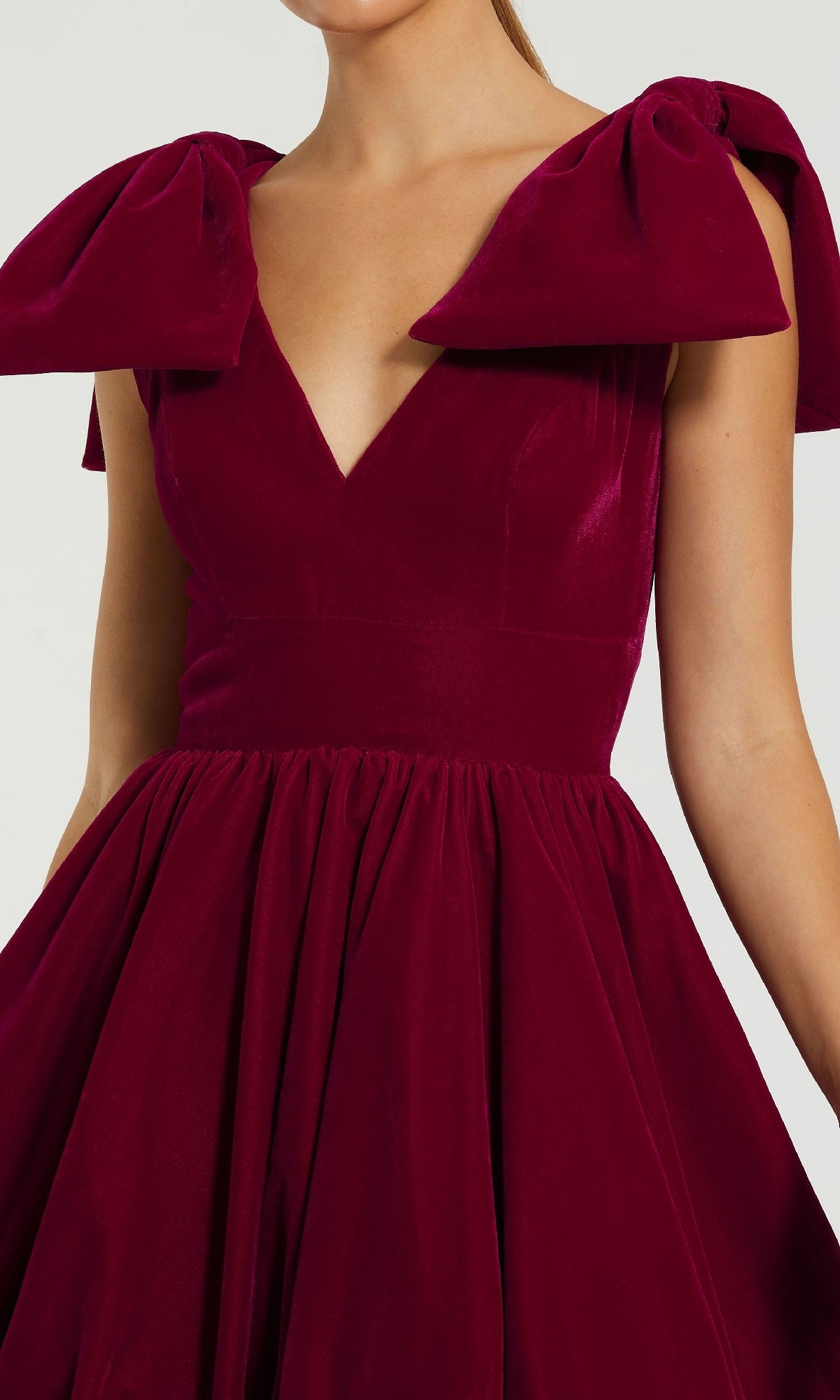 A woman wears the Mac Duggal 11743 Berry Red Mini Semi-Formal Dress, featuring a V-neckline, deep red velvet fabric, and bold bow details on the shoulders—a stunning cocktail choice.