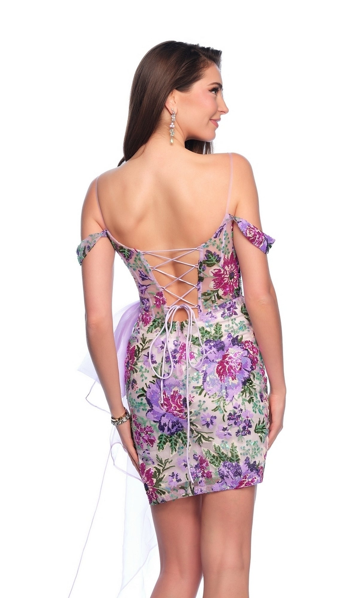 A woman in the Dave & Johnny Purple Print Hoco Dress 11770, a short off-shoulder floral dress with a corset bodice and lace-up open back, stands facing away.
