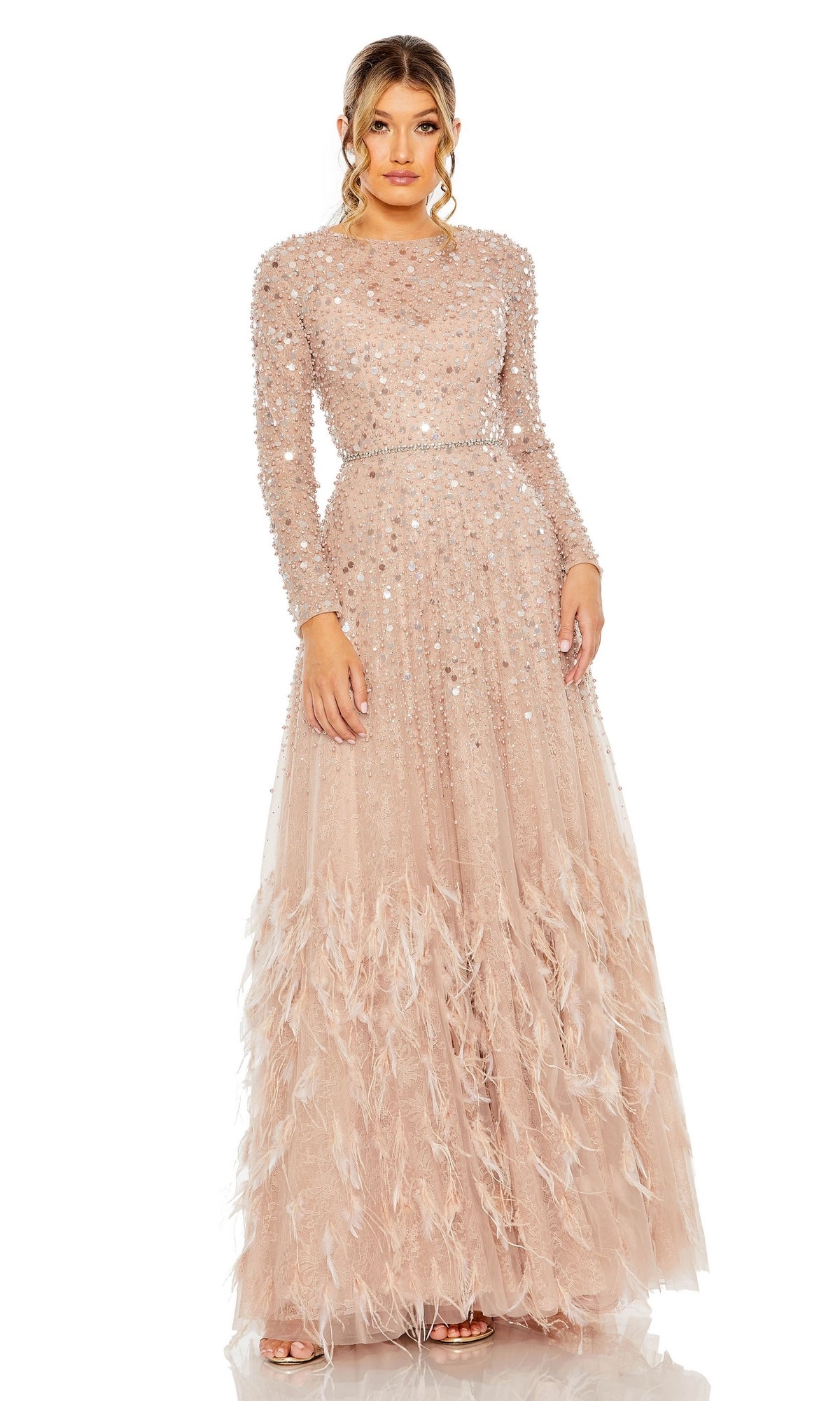 A woman wears the Mac Duggal 11782 Long Sleeve Sequin Formal Gown in blush, featuring pearl embellishments and a feathered skirt hem—an elegant mother of the bride dress—while standing against a plain white background.
