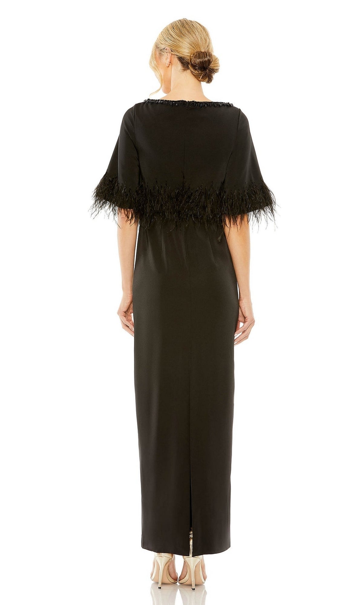 A woman with blonde hair in a low bun wears the Mac Duggal 11787 short-sleeve black formal dress, viewed from the back and standing in high-heeled shoes.