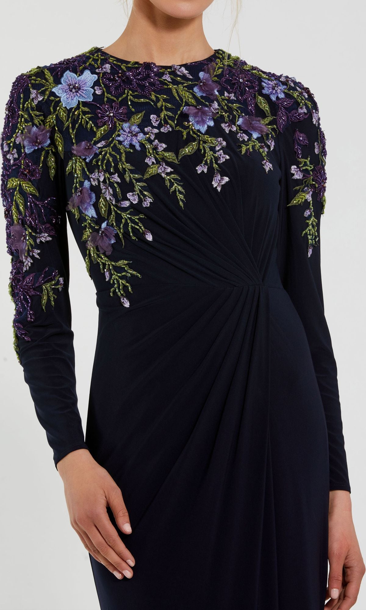 A woman in the Mac Duggal 11806 Long Sleeve Blue Formal Dress, featuring purple and green floral embroidery on the shoulders and chest and gathered fabric at the waist.