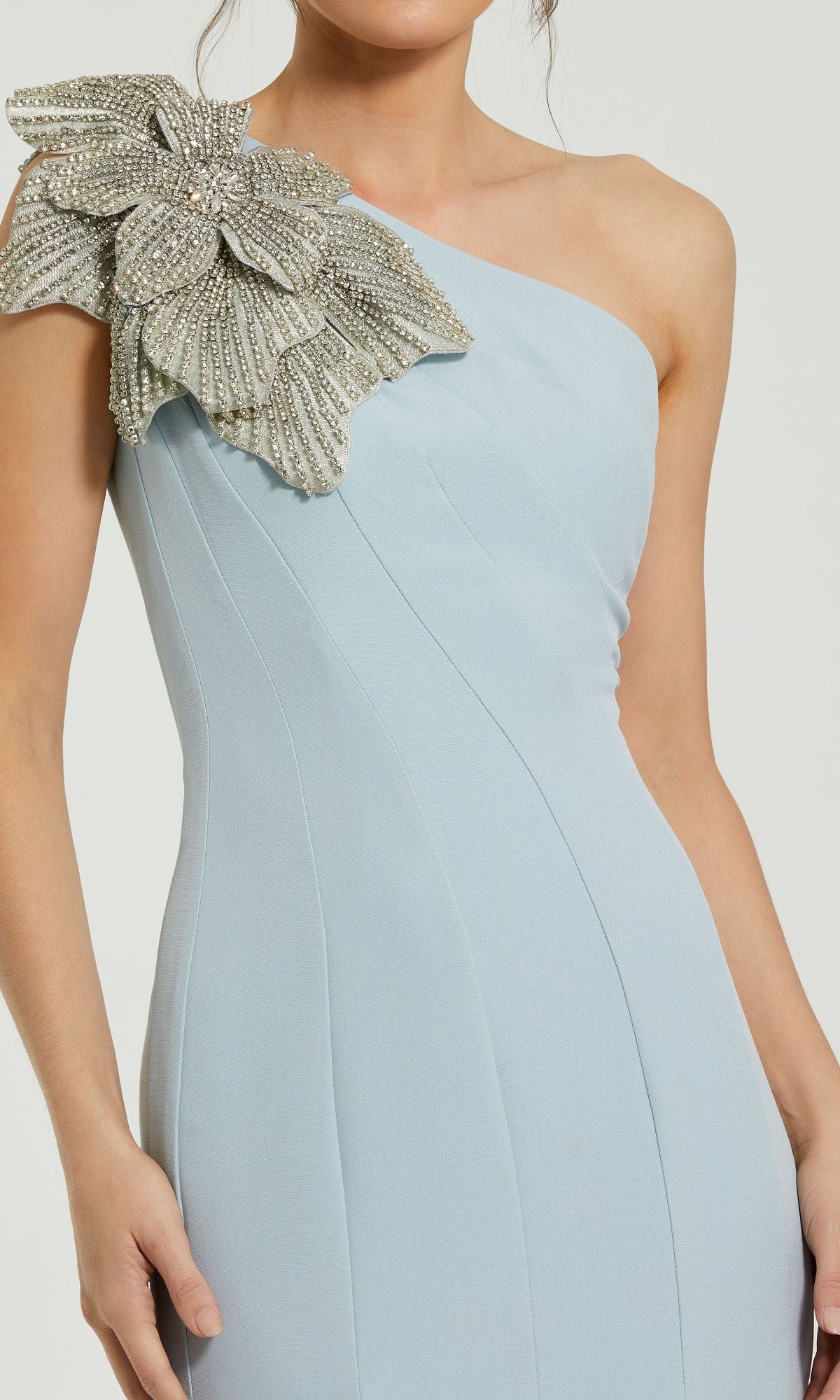 A woman wears the Beaded-One-Shoulder Prom Gown: Mac Duggal 11810, a stunning light blue formal dress with a large silver beaded floral embellishment on one shoulder—perfect for prom or evening events.