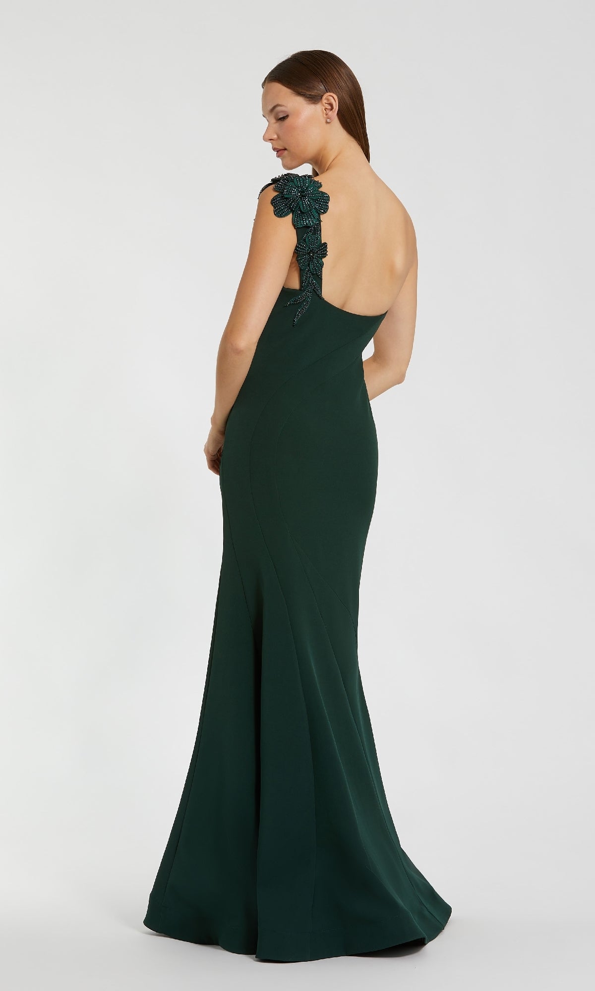 Woman wearing a dark green evening gown with floral details on a white background