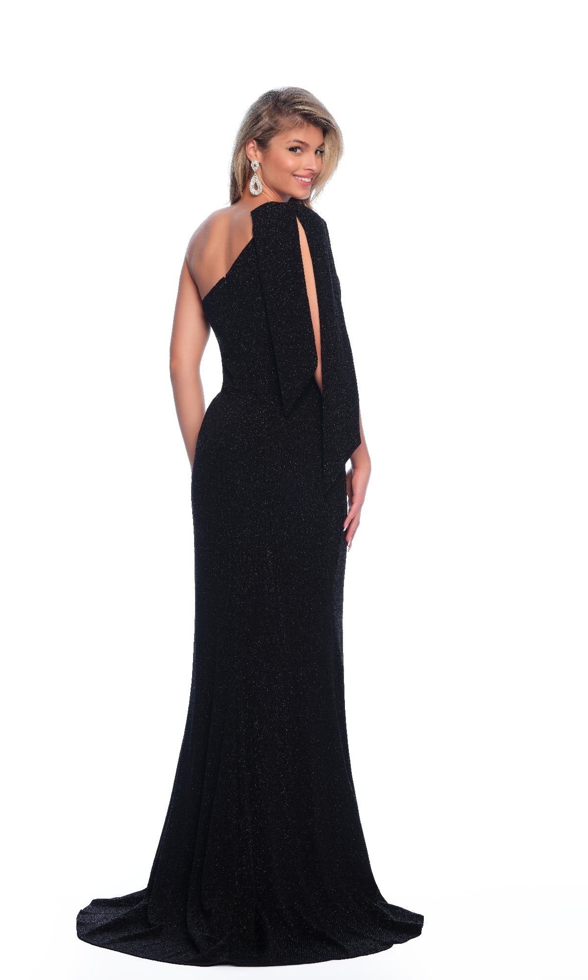 A woman stands against a white background, looking over her shoulder in the Dave & Johnny 11851 one-shoulder black prom dress, featuring glitter fabric and a bow detail on the back.