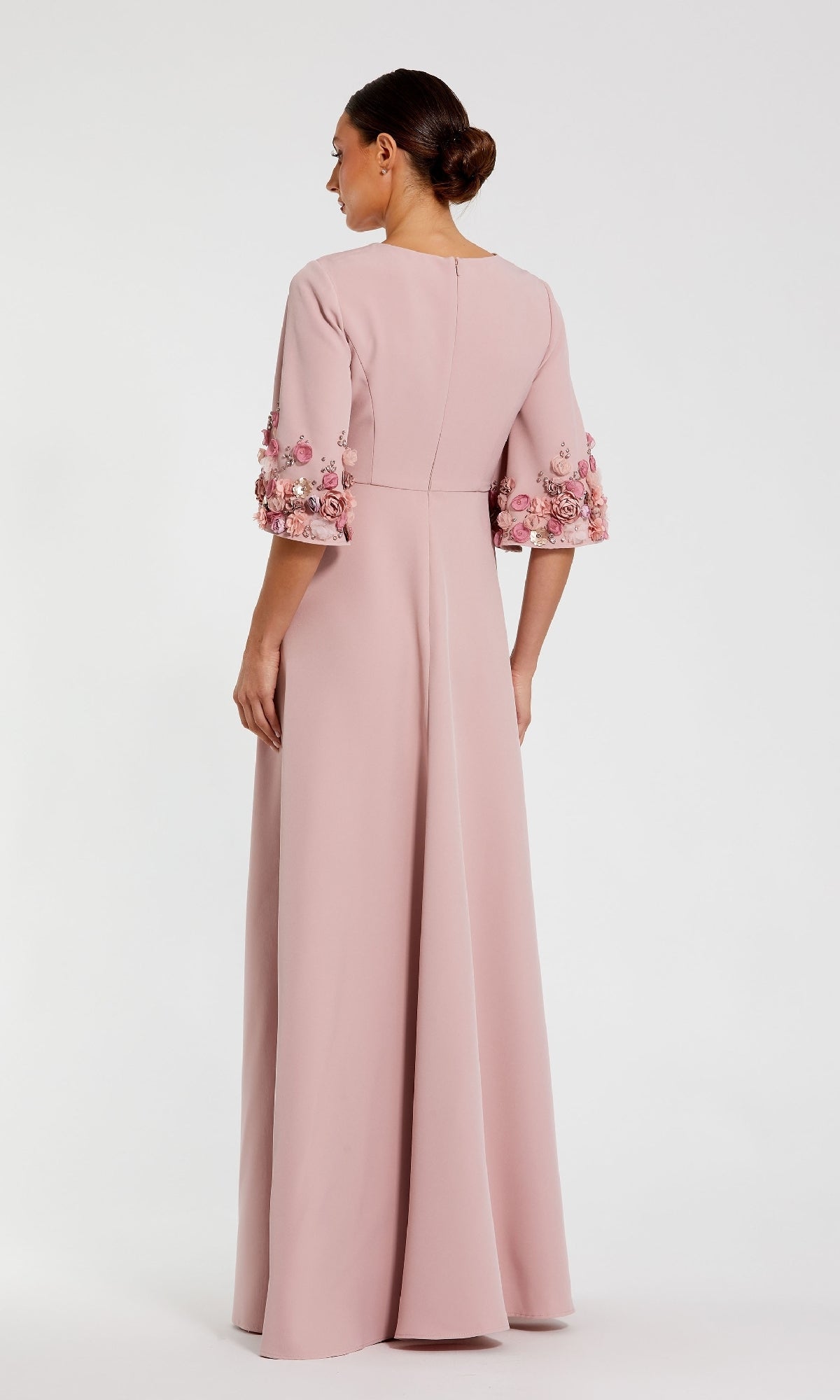 A woman is shown from the back wearing the Mac Duggal 11854 Bell-Sleeve Long Formal Dress, a floor-length pale pink gown with floral appliqués and modest elbow-length bell sleeves, set against a plain white background.