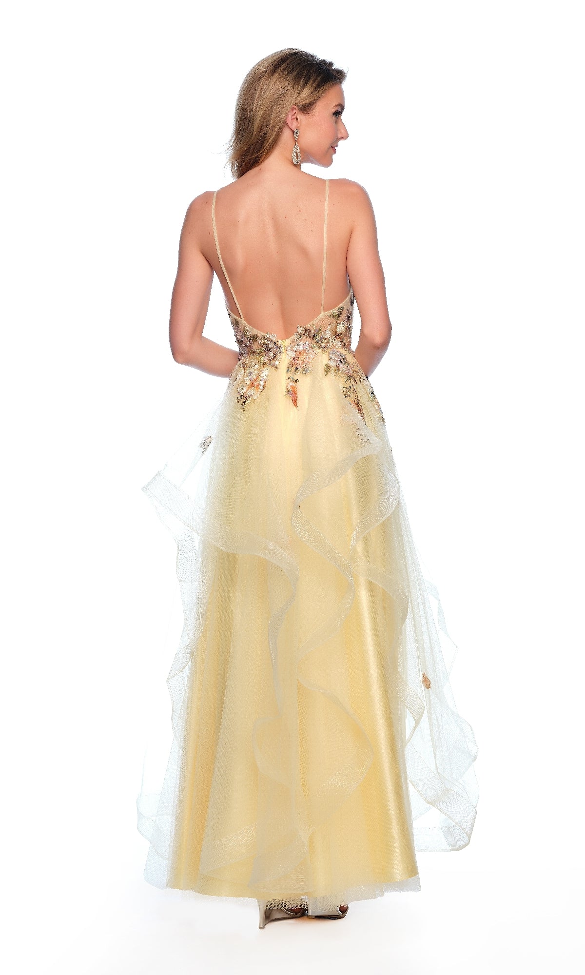 A woman stands facing away in the Long Yellow Prom Dress: Dave & Johnny 11859, featuring a sleeveless, backless design with floral appliqué, ruffled layers, and a horsehair hem tulle skirt for graceful volume.