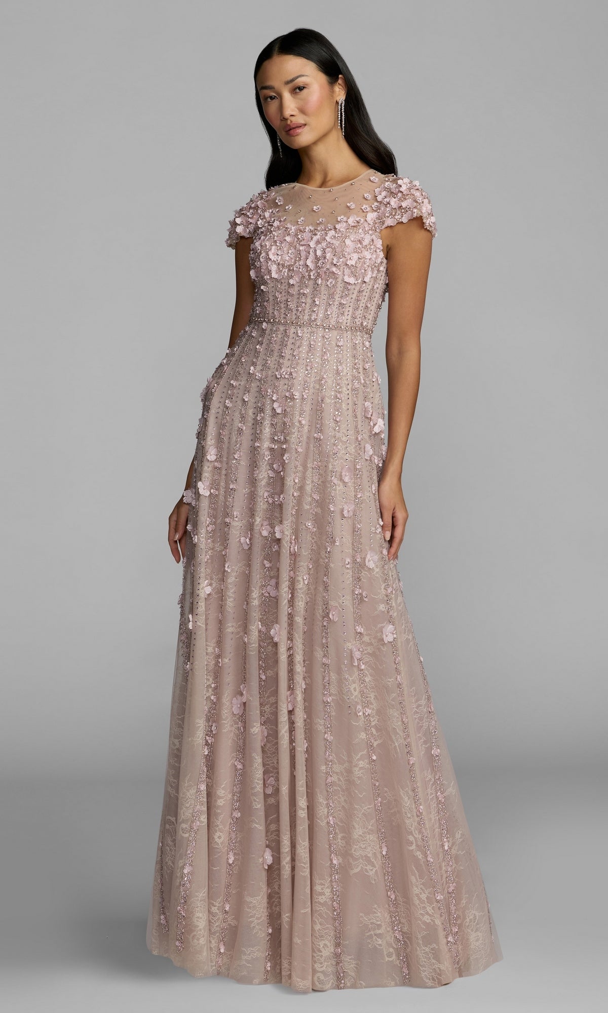 A woman wearing a floor-length, vintage lilac gown adorned with beading and featuring a fitted bodice, reminiscent of the Mac Duggal 11866 Long Beaded Lilac Formal Dress, stands against a plain gray background.