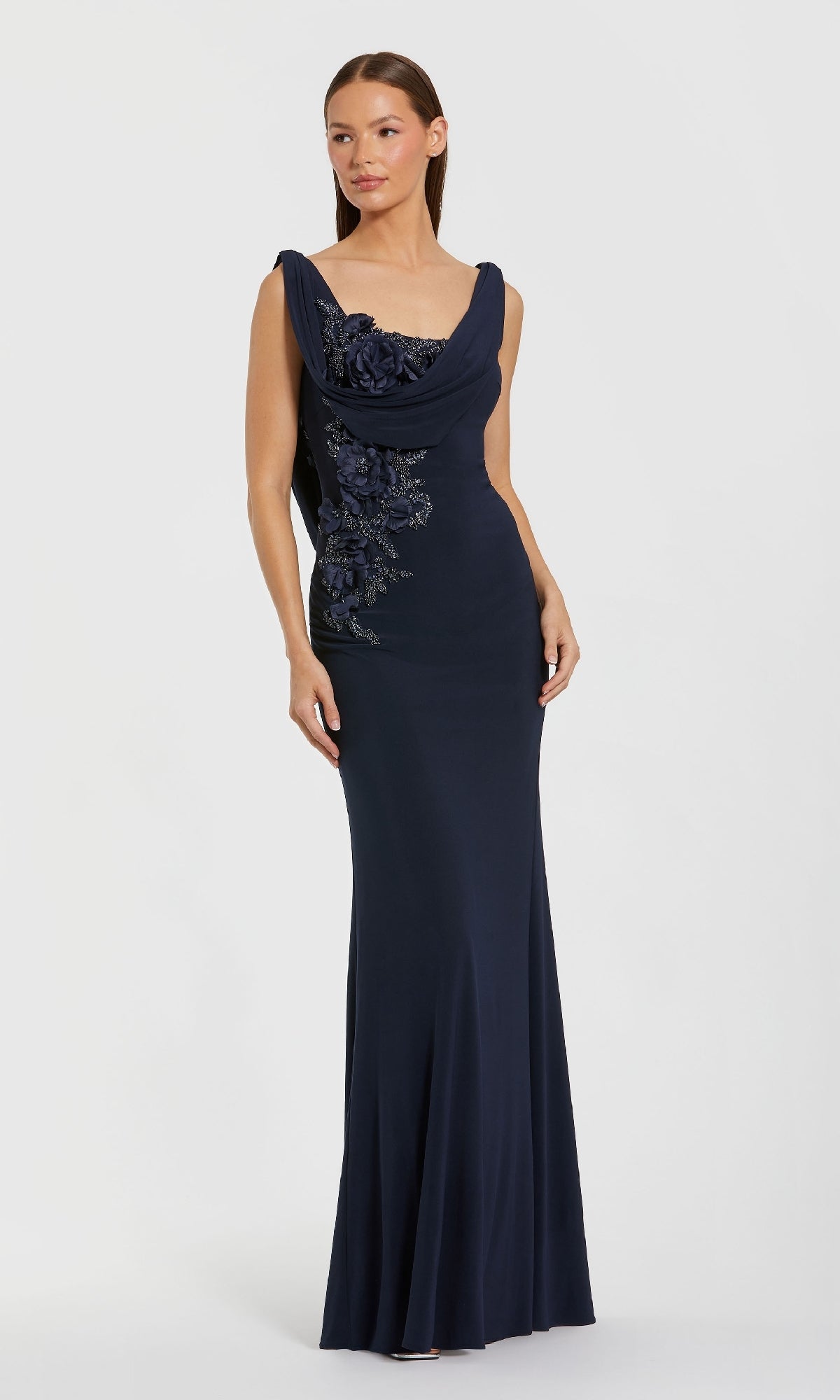 A woman models the Mac Duggal 11910 Cowl-Neck Long Formal Dress, a navy blue evening gown with floral embellishments, against a simple light background.