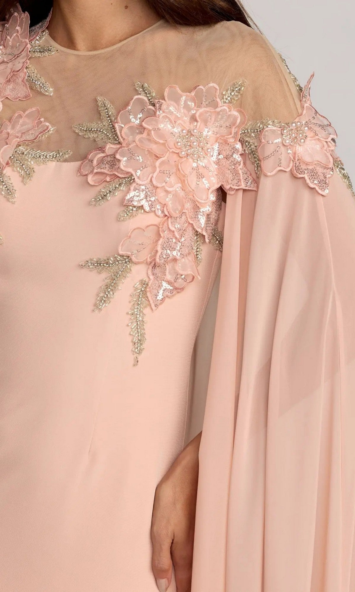 A close-up of the Mac Duggal 11942 Long Formal Dress in light pink, featuring sheer fabric at the neckline adorned with pink 3D floral appliqués and sequin embellishments on the shoulder. The flowing, loose sleeve beautifully complements this elegant long formal dress.