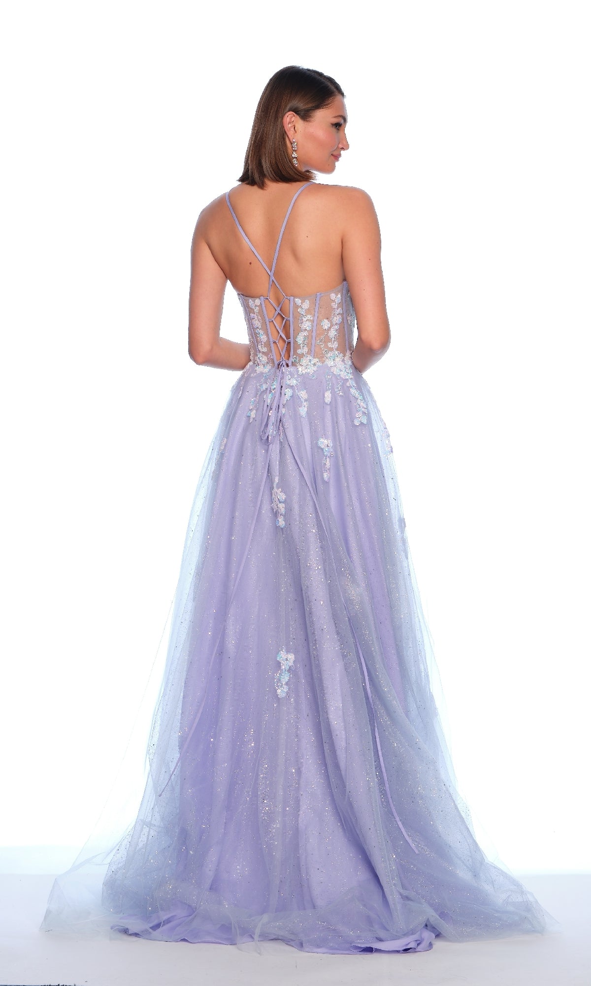 A woman models the Dave and Johnny 12015 long prom dress with light purple 3D flowers, a lace-up sheer back, and an embroidered lace corset bodice, standing gracefully against a white background.