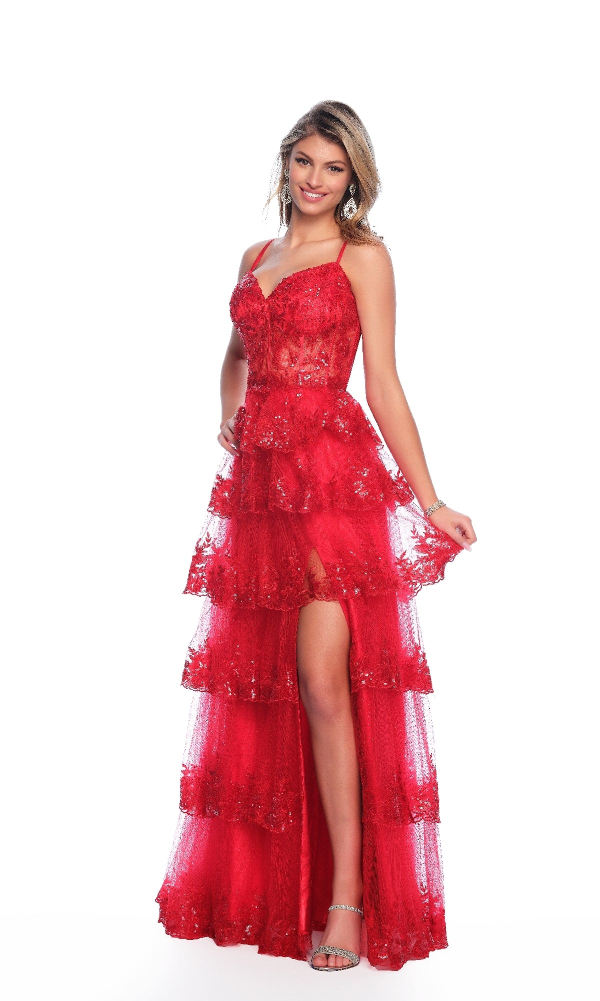 A woman smiles in the A-Line Red Prom Dress: Dave and Johnny 12051, featuring a sweetheart neckline, tiered lace skirt, and thigh-high slit, standing against a white background.