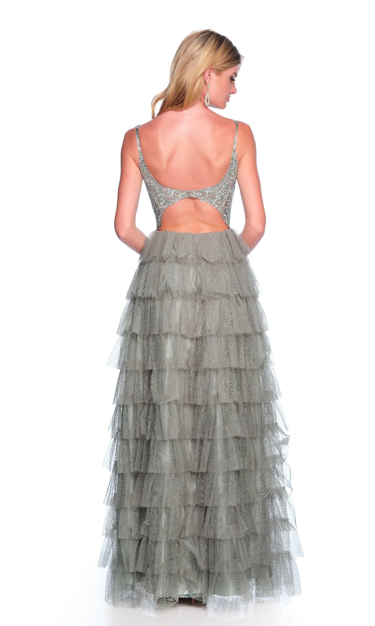 A woman wears the Dave and Johnny 12053 long prom dress in silver, featuring a ruffle-tiered skirt, spaghetti straps, and a low-cut back as she stands facing away from the camera.