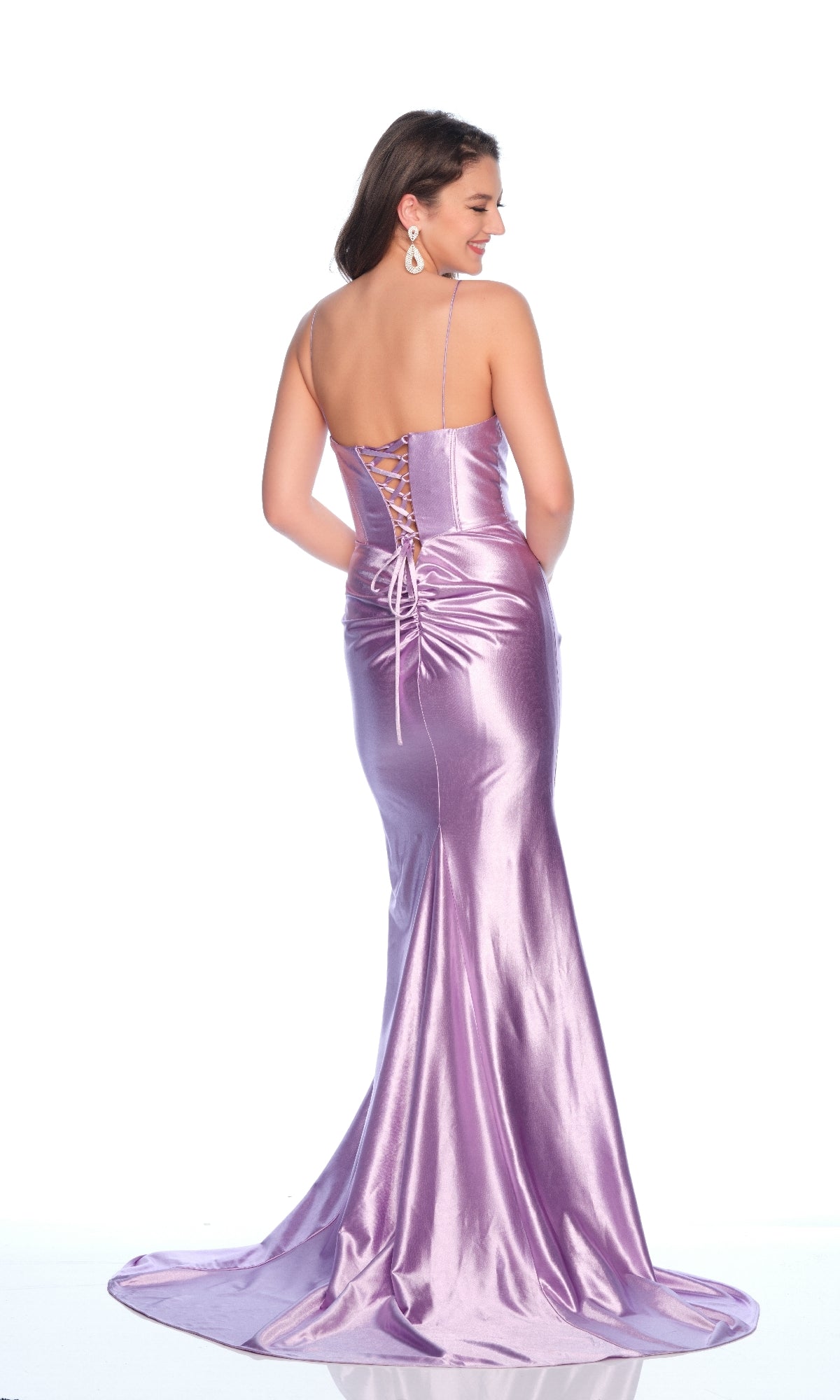 A woman wears the Dave and Johnny 12220 long prom dress in metallic lilac, featuring thin straps and a lace-up back, as she stands facing away from the camera.