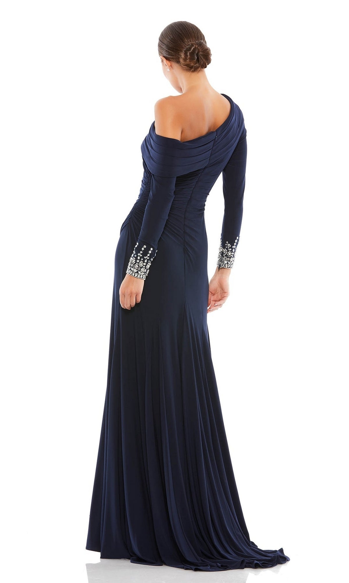 A woman stands facing away, wearing the Mac Duggal 12231—an elegant one-shoulder long formal dress in dark blue, floor-length and sophisticated.