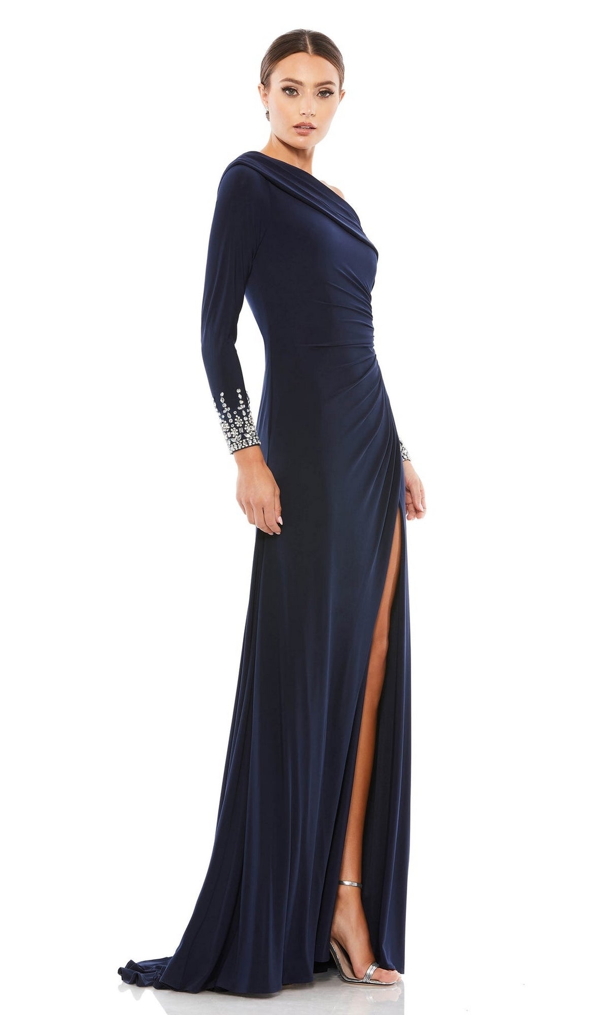 A woman stands elegantly in a studio, wearing the Mac Duggal 12231 one-shoulder long formal dress—an evening gown with silver-embellished cuffs, navy blue fabric, and a high slit.