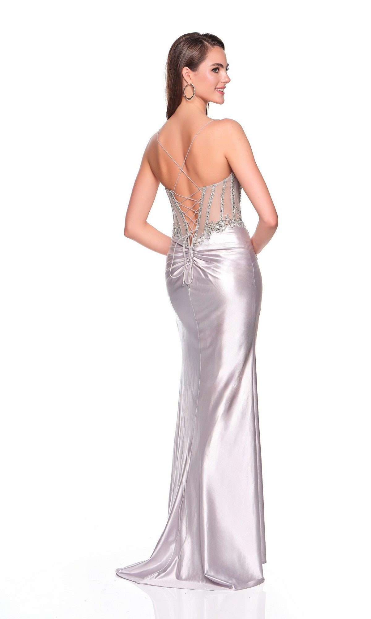 A woman in the Long Sleek Prom Dress: Dave & Johnny 12239, featuring silver satin, a lace-up back, and thin straps, stands facing away while smiling over her shoulder.