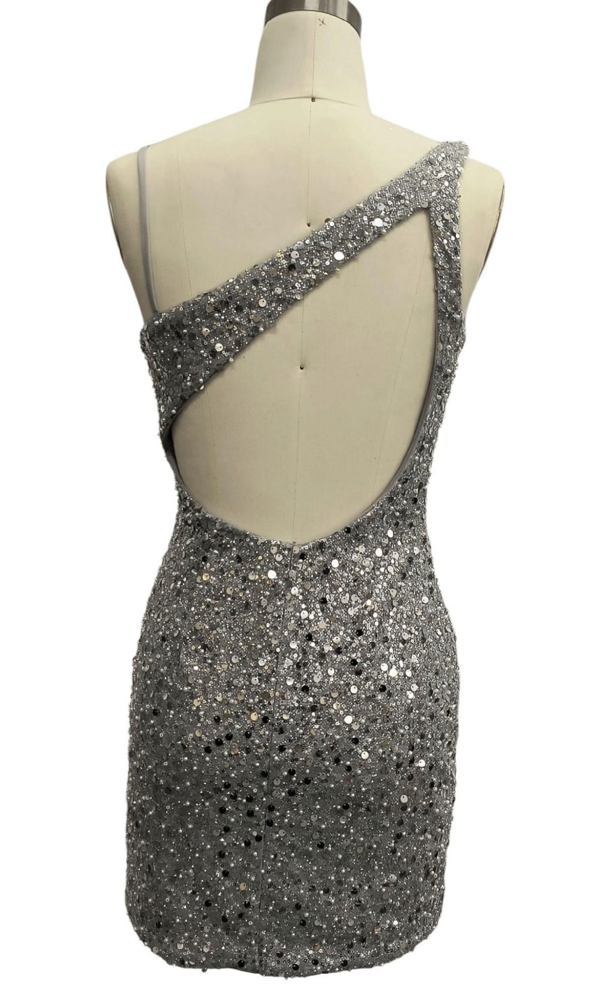 Back view of mannequin in Short Silver Homecoming Dress: 12353, featuring an asymmetrical neckline, one-shoulder strap, dramatic open back, and shimmering silver sequins.