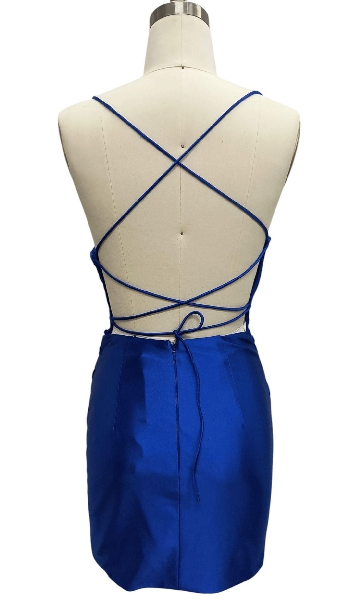 A mannequin displays the Royal Blue Mini Hoco Dress: 12383, featuring a low back, crisscross spaghetti straps, a tied waist, and a 3D flower hemline.