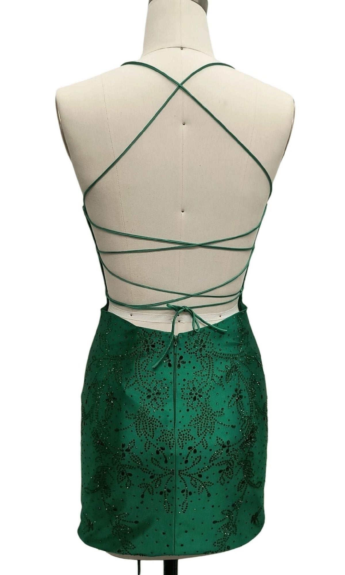 A mannequin models the Tight Green Short Hoco Dress: 12414—featuring crisscross spaghetti straps, beaded accents, and a backless design, this party dress is perfect for making a statement at any event.