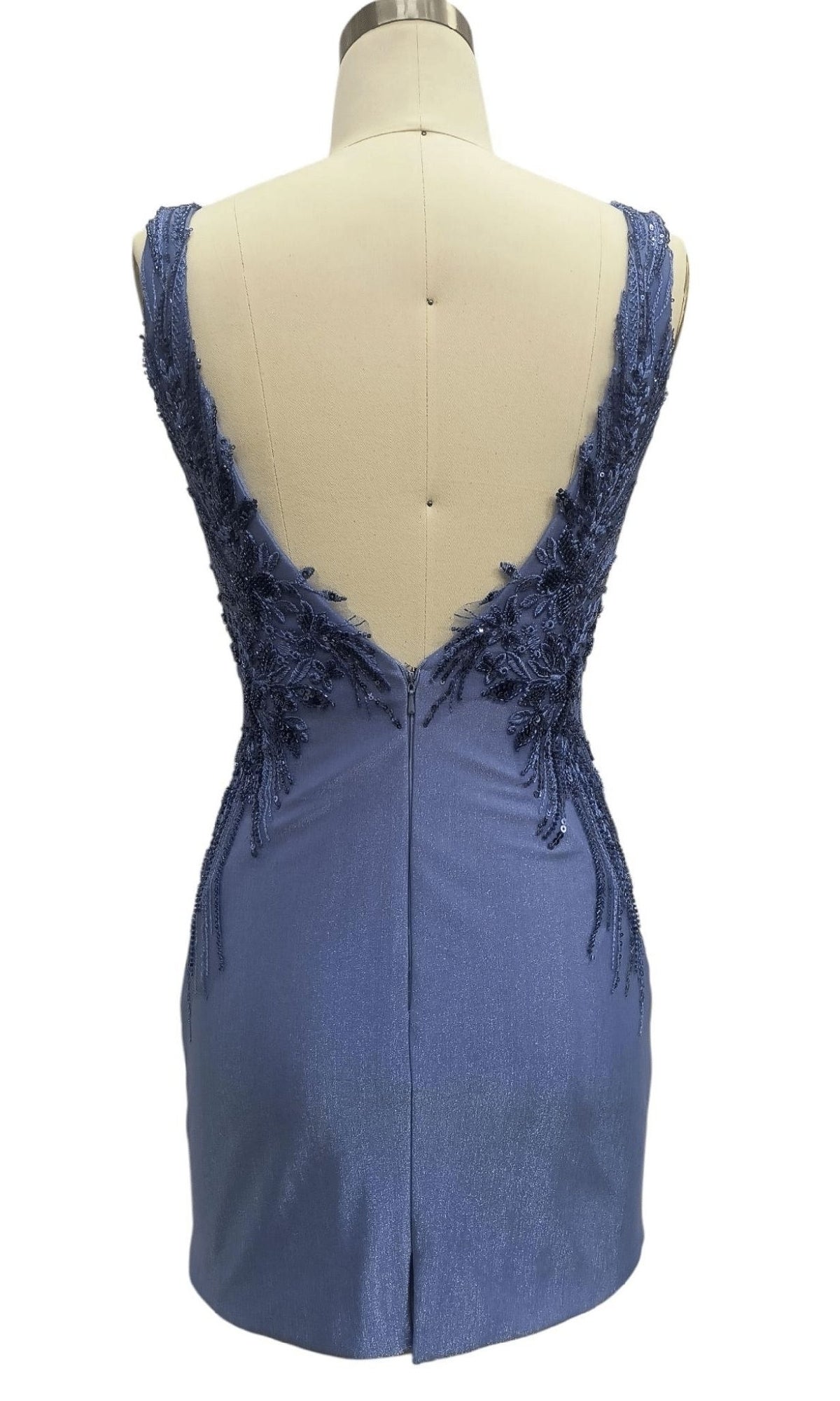 The V-Back Short Blue Hoco Dress: 12462 is a sleeveless, short blue dress with a deep V-back, adorned with floral lace and beaded appliqué on the upper back, shown on a dress form.