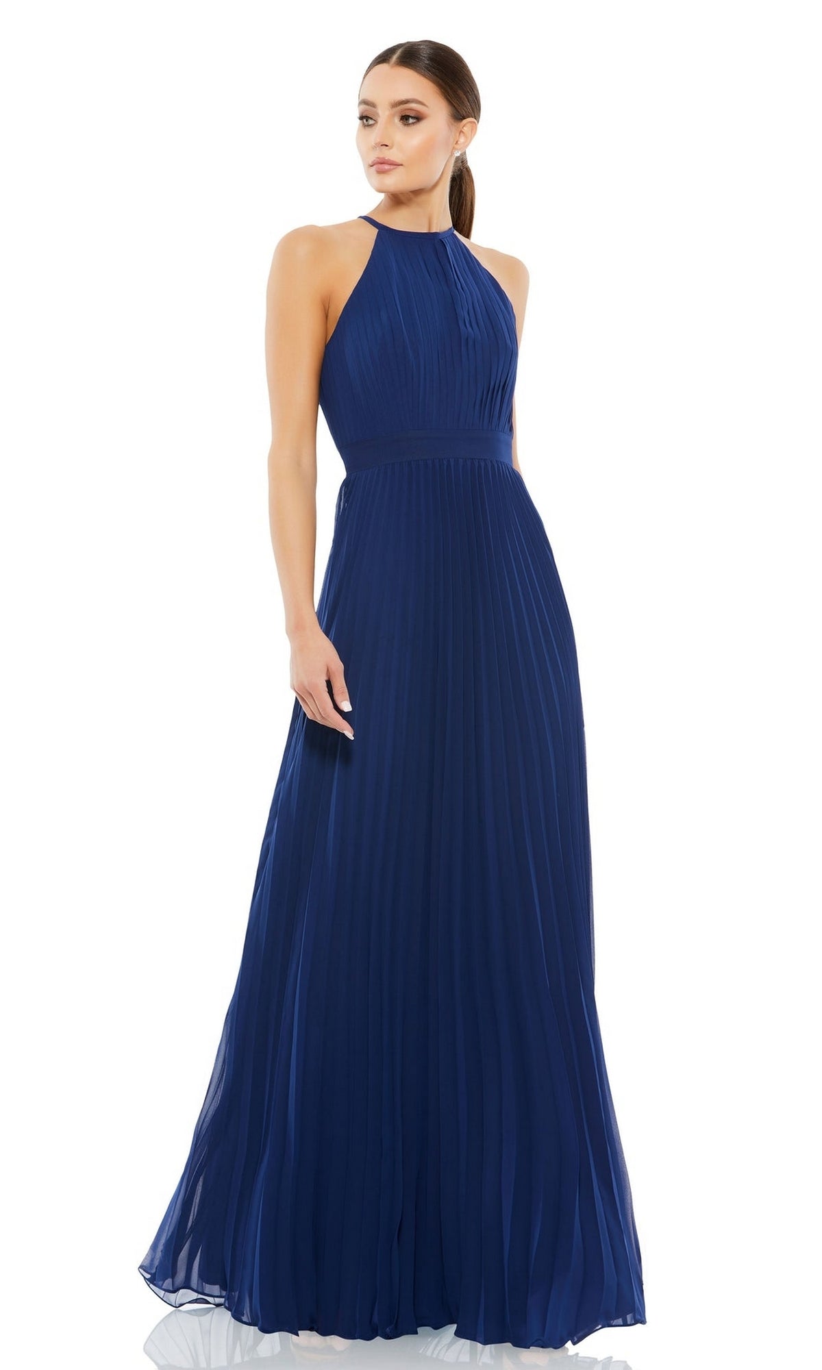 A woman wearing the Long Formal Dress 12496 by Mac Duggal—a sleeveless, floor-length, navy blue pleated gown with a high neckline—stands against a white background.