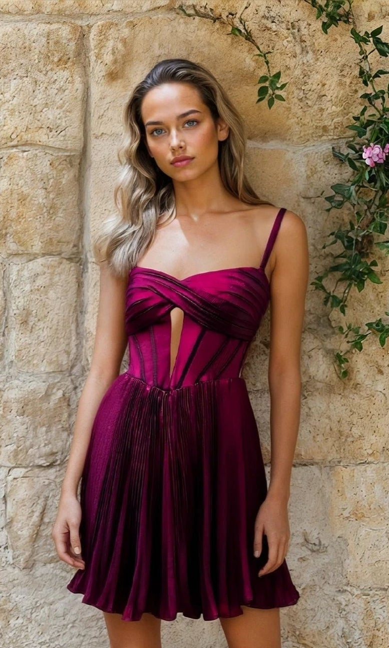 Woman stands against a stone wall, wearing the Fuchsia Pink Short Hoco Dress: 12511, featuring a sleeveless pleated skirt and corset-inspired cut-out bodice.