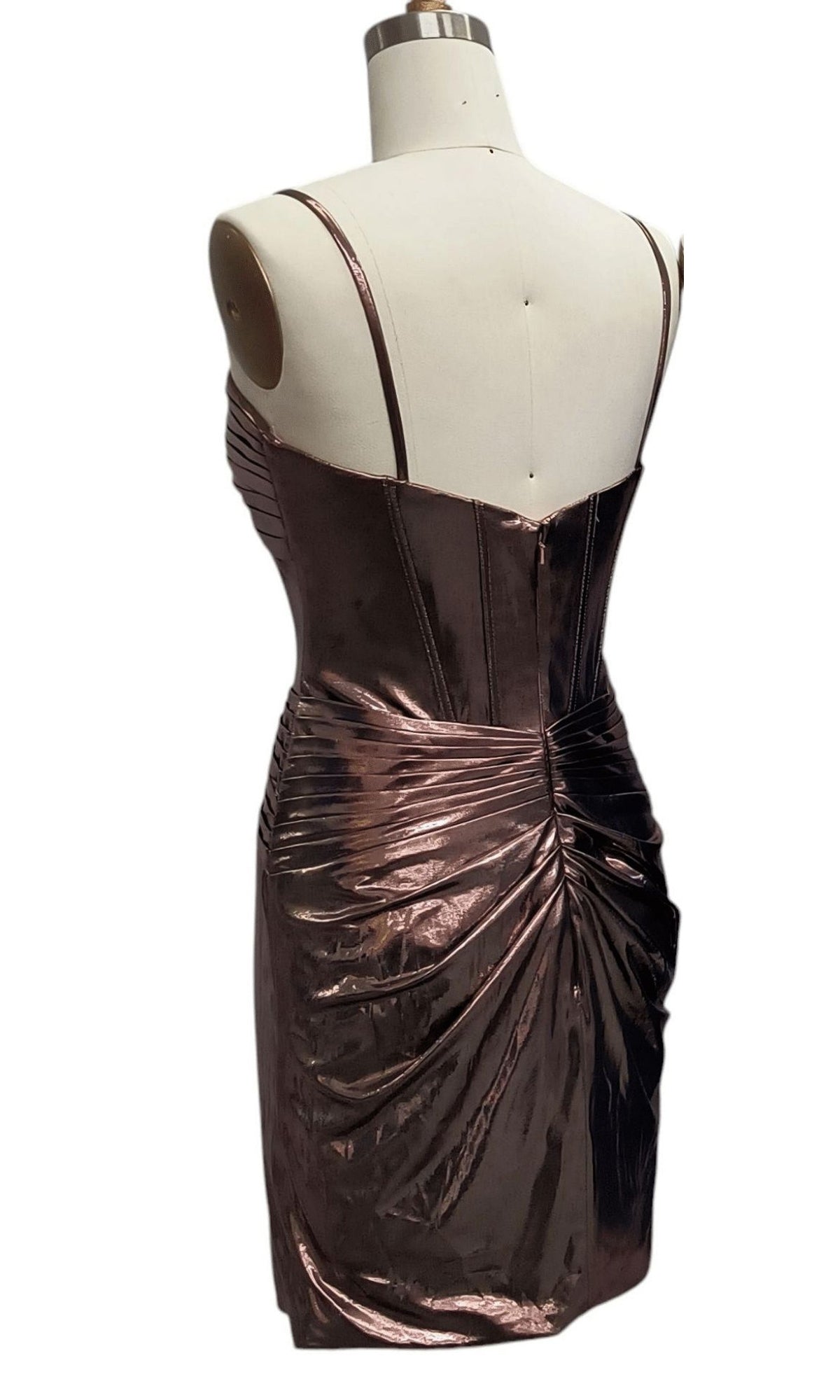 A back view of the Cut-Out Short Metallic Hoco Dress 12512 in metallic bronze, featuring thin straps, ruched detailing, and a corset-style bodice on a dress form.