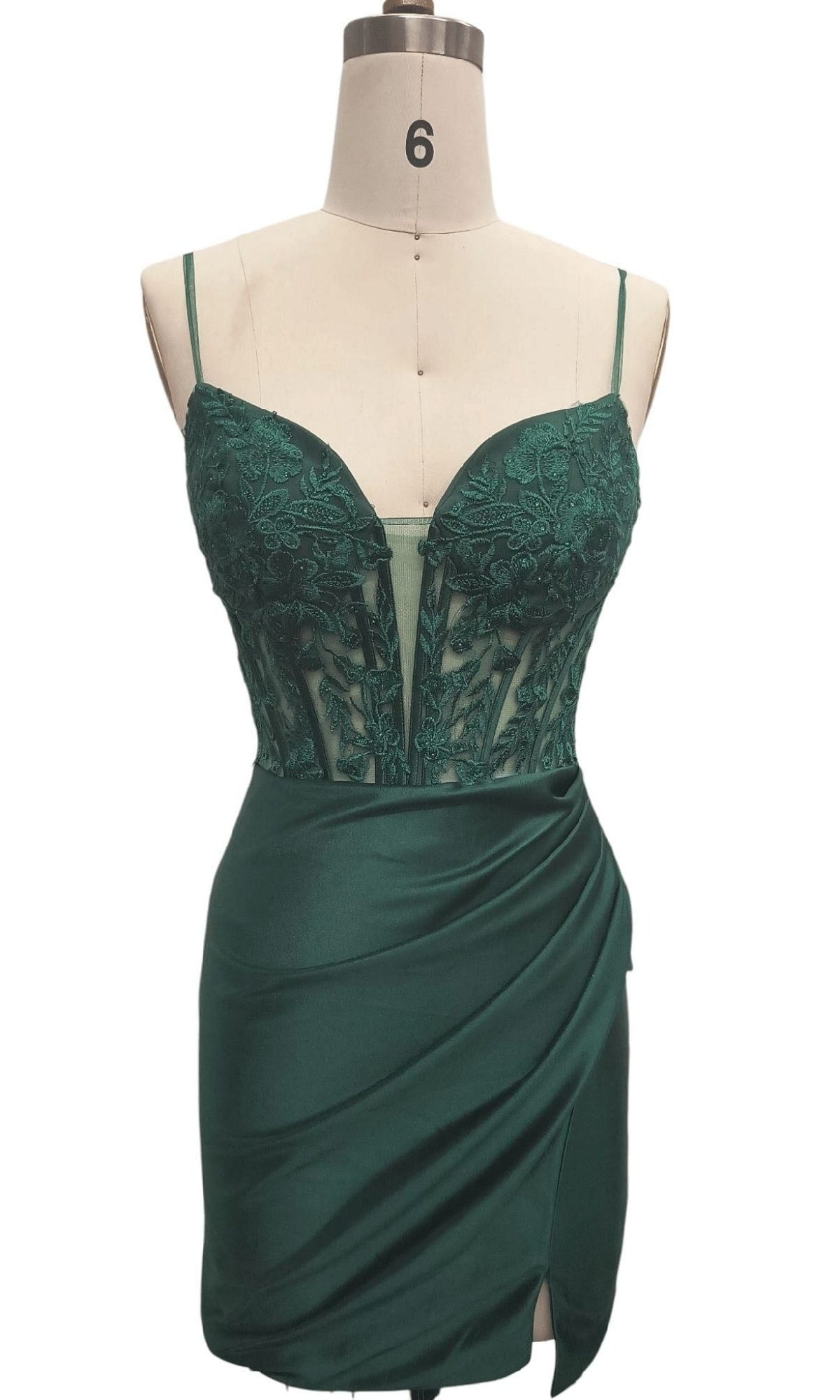 The Dave & Johnny 12583 short homecoming dress in emerald green features thin straps, a floral lace embroidered bodice, and a draped satin skirt with a slit, displayed on a mannequin.