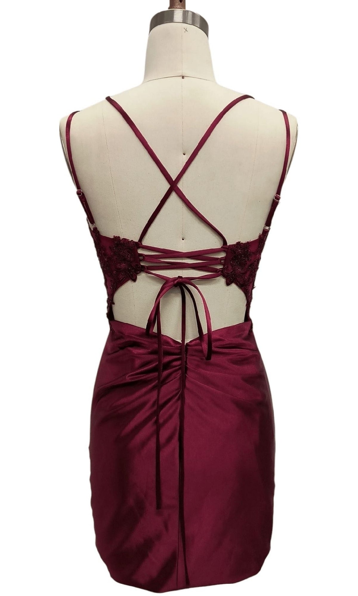 Back view of the Dave & Johnny 12619 short burgundy hoco dress, shown on a mannequin. Features satin with lace details, crisscross strappy back, and a lace-up waist—ideal as a chic homecoming dress.
