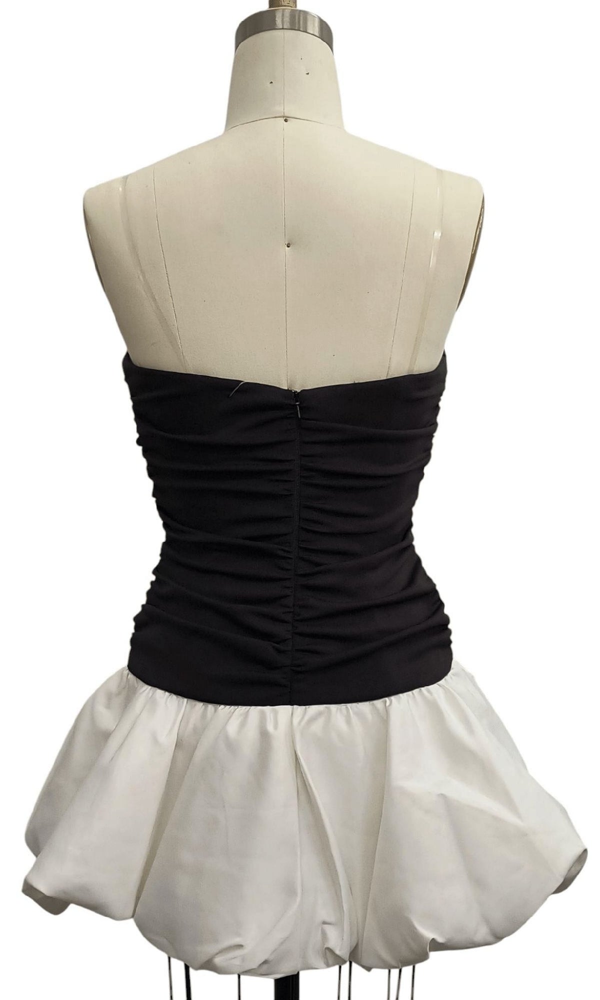 A dress form displays the Black and White Hoco Dress: 12656, featuring a strapless ruched black bodice and a voluminous white bubble skirt, shown from the back—a striking party dress.