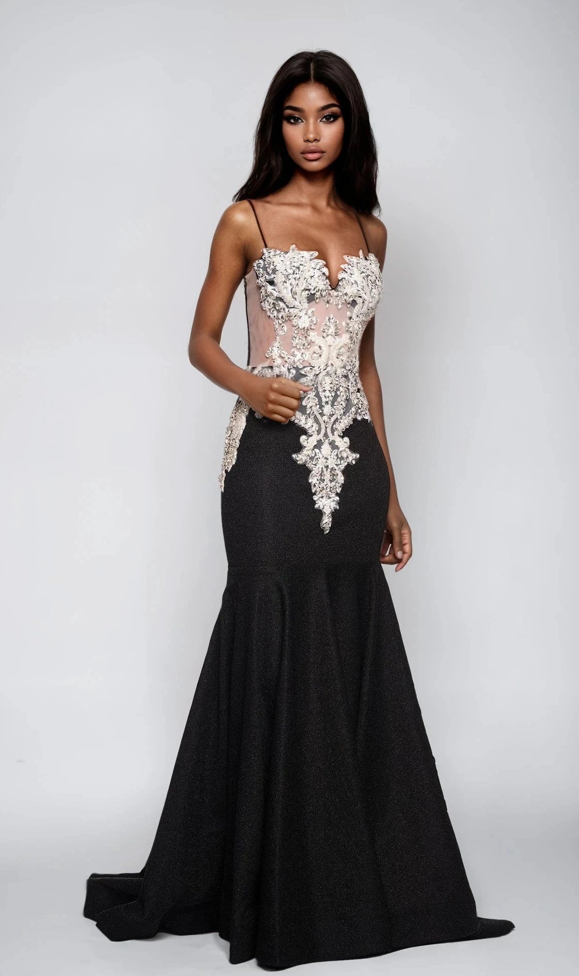 A woman models the Dave and Johnny 12800 long black prom dress featuring a fitted silhouette and sheer front bodice with white floral appliqué, standing against a plain light gray background.