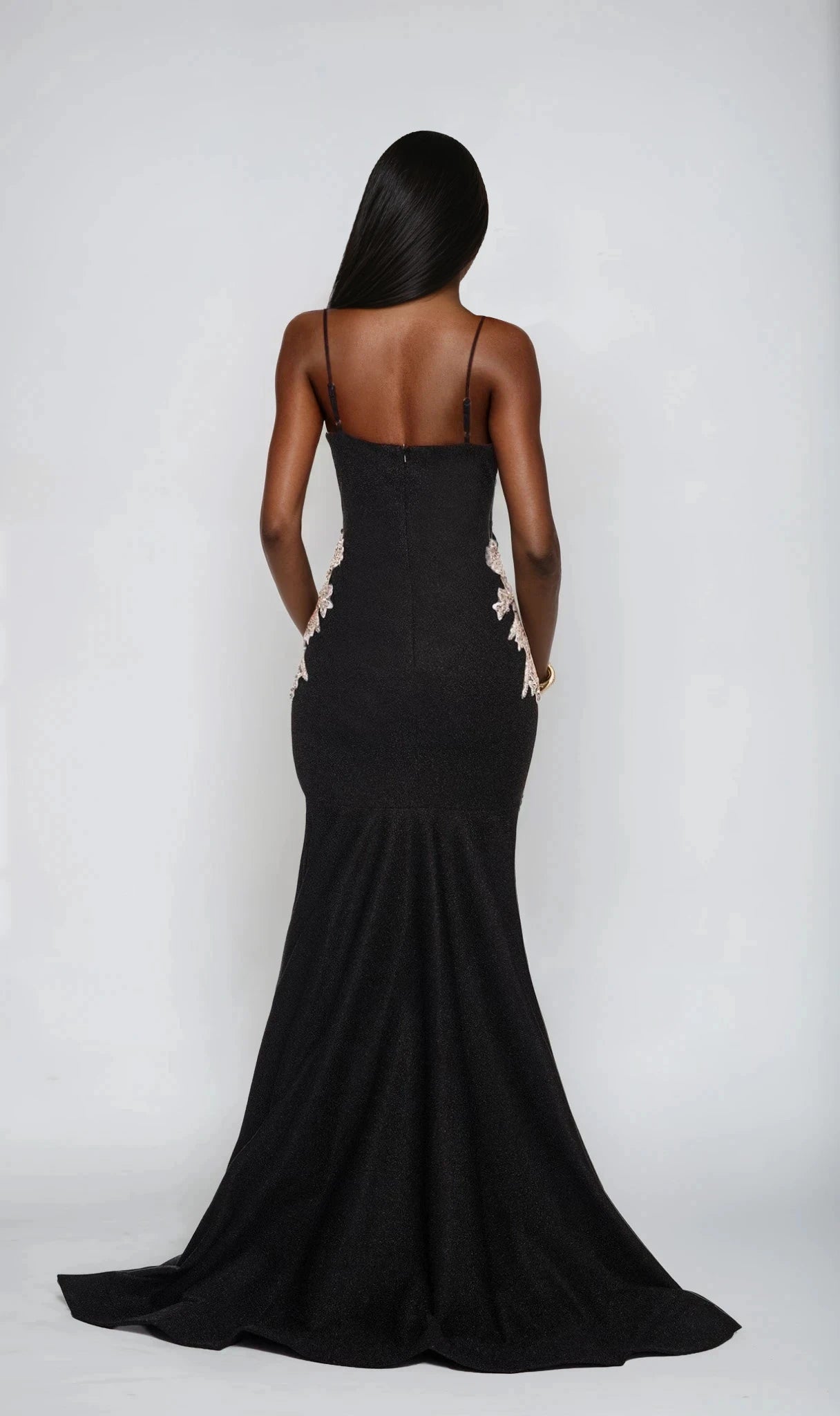 A woman faces away, wearing the Dave and Johnny 12800 long black prom dress with thin straps and floral embellishments at the hips.