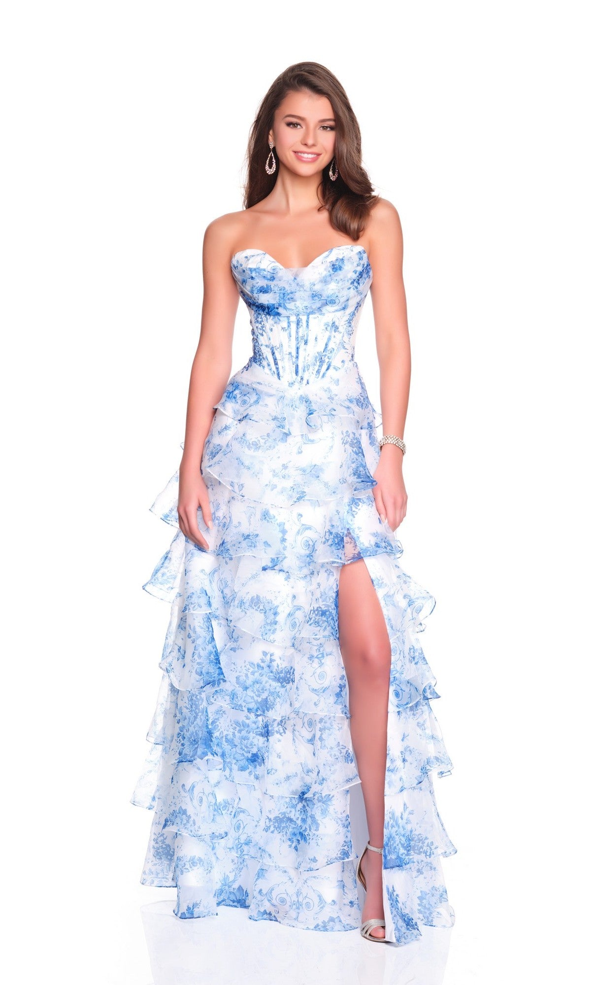 A woman models the Dave and Johnny 12936 long prom dress—blue floral print, strapless, with a high slit and tiered ruffles—styled with hoop earrings and high-heeled sandals against a white background.