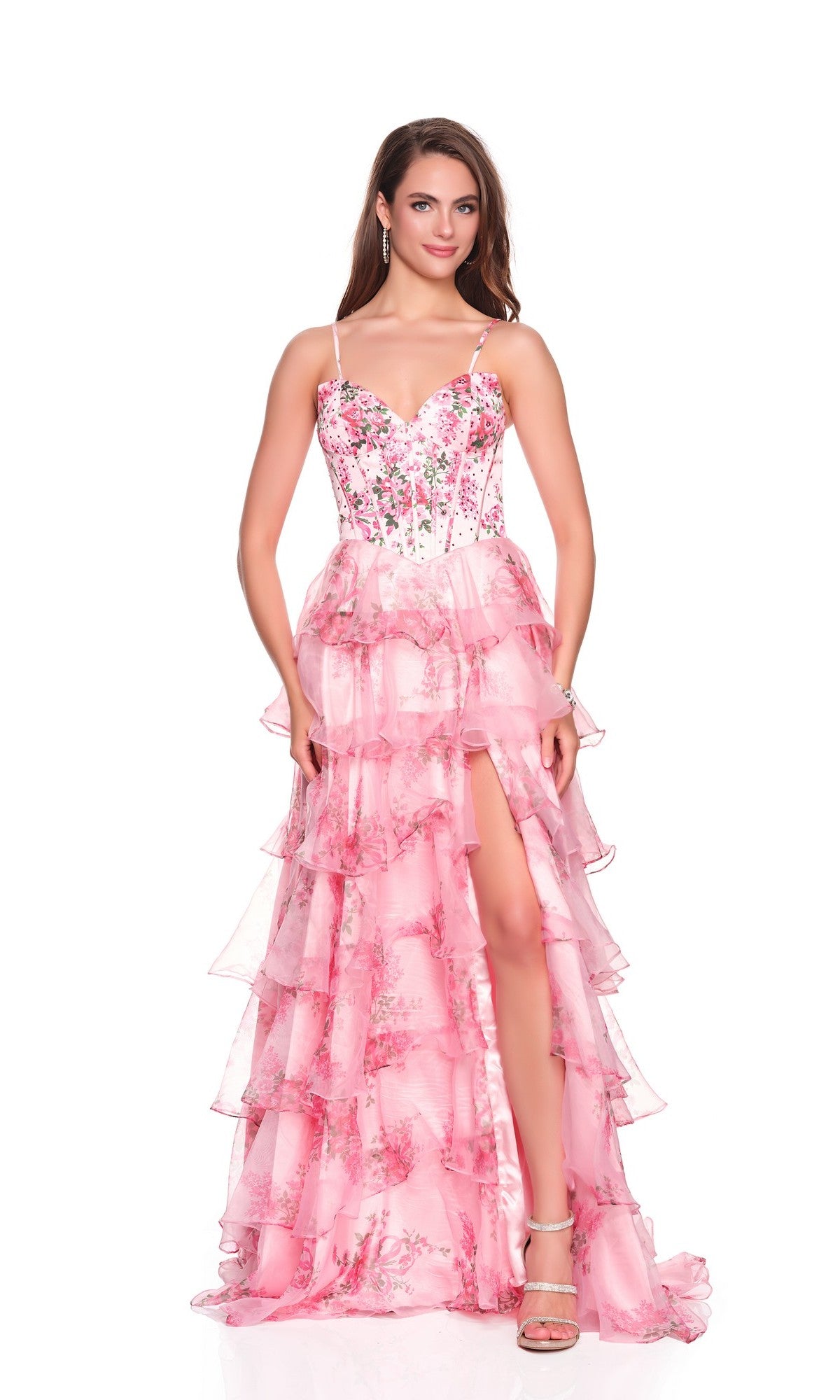 A woman models the Dave and Johnny 12941 long prom dress featuring a beaded satin corset bodice, thin straps, ruffled details, and a high-slit chiffon A-line skirt in pink, standing against a white background.