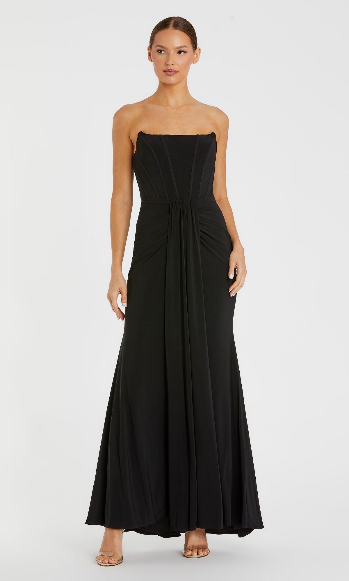 A woman stands against a plain white background wearing the Mac Duggal 13003— a strapless long black formal dress featuring a fitted bodice and draped skirt.