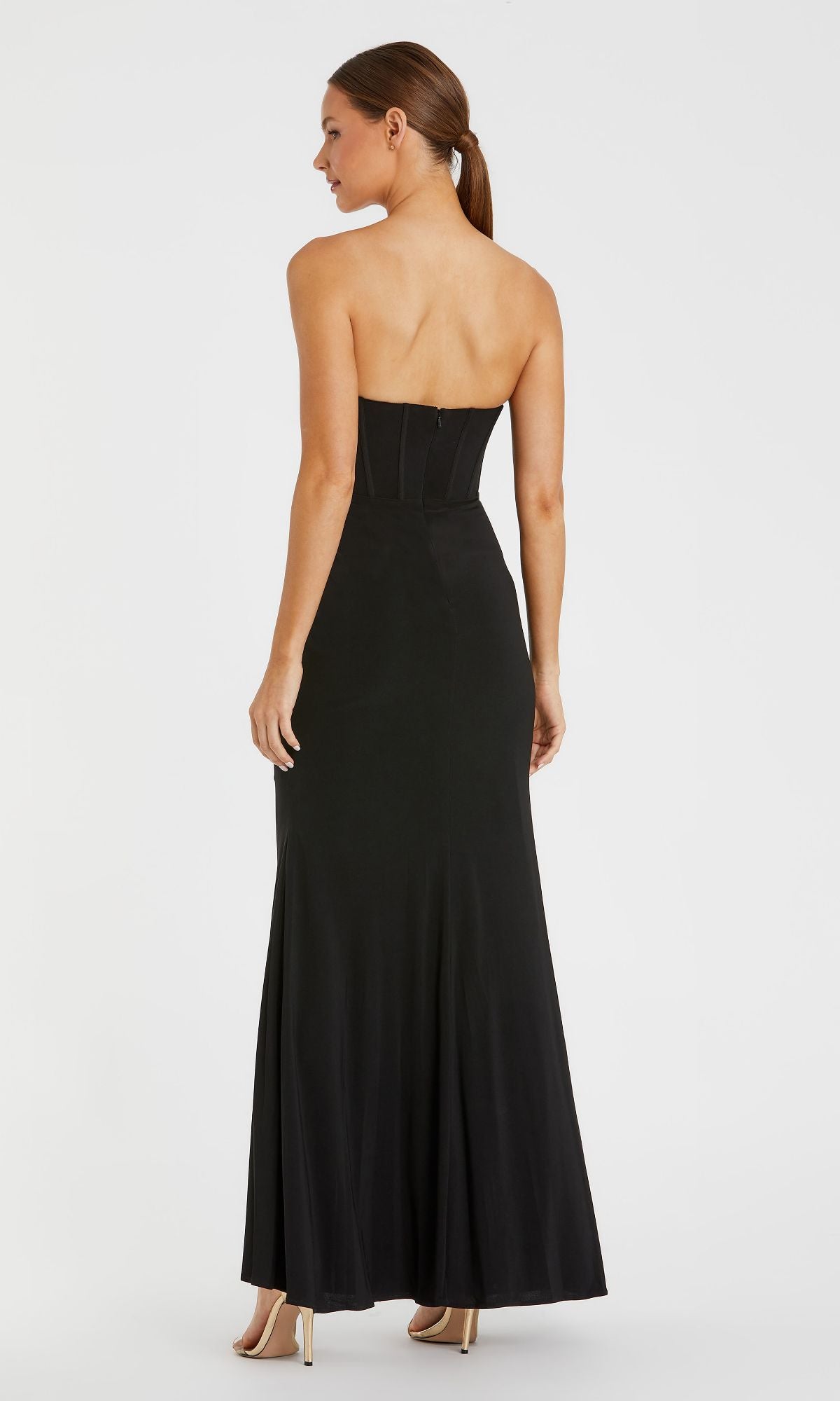A woman stands facing away, wearing the Mac Duggal 13003 Strapless Long Black Formal Dress and beige high heels against a plain white background.