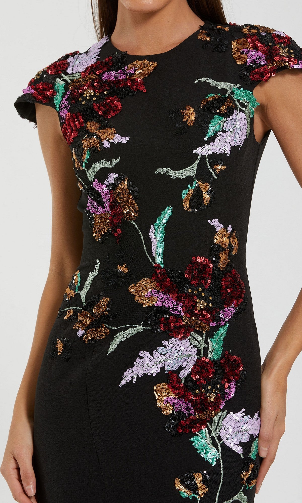 A woman wearing the Mac Duggal 13211 long formal dress, a fitted black crepe trumpet gown featuring vibrant floral sequin embroidery on the bodice and sleeves.