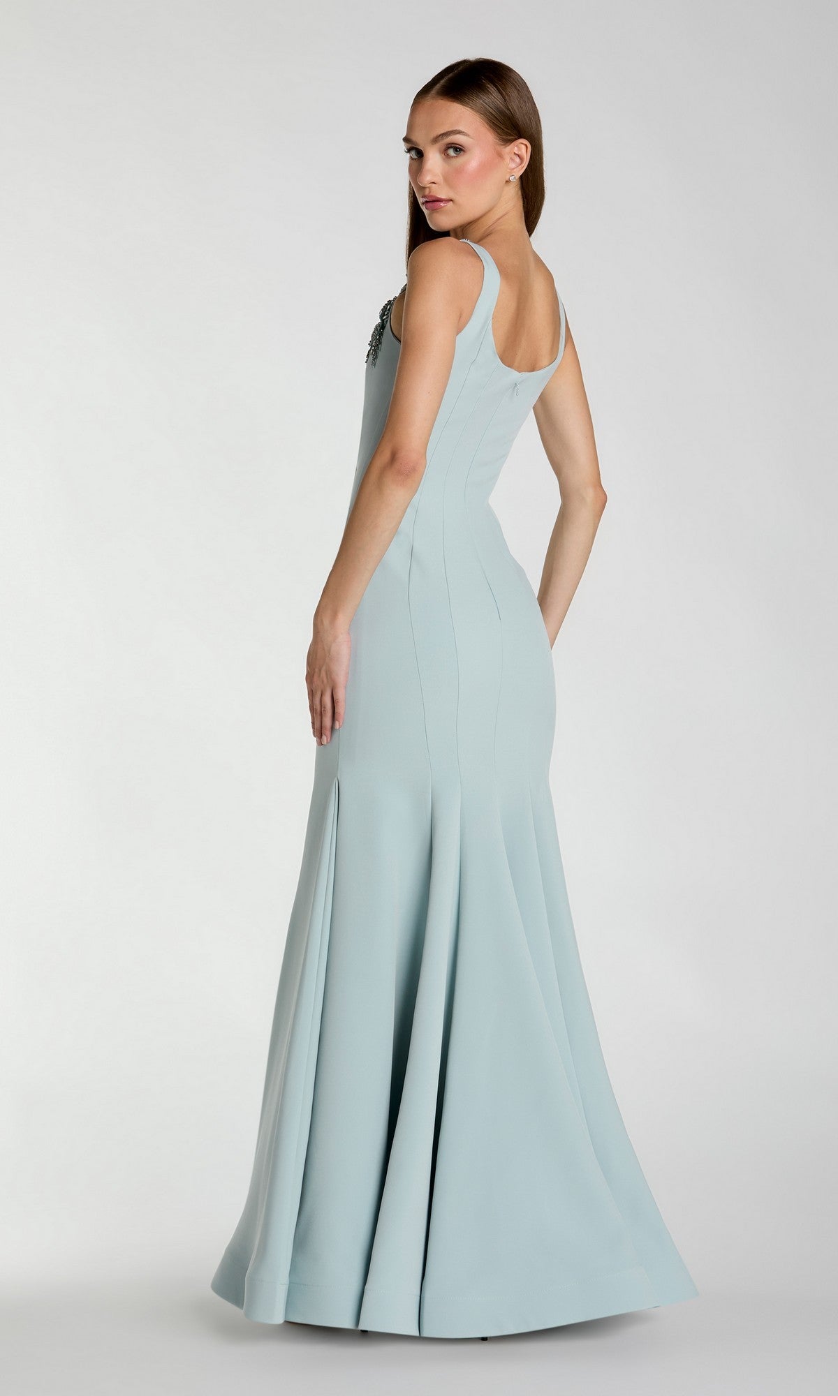 A woman models the Mac Duggal 13224 Long Formal Dress, a light blue, sleeveless, floor-length mermaid gown, posing with her back slightly turned and head looking over her shoulder against a plain white background.