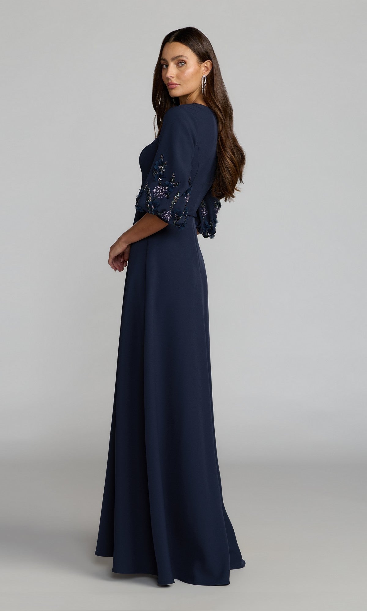 Woman in the Mac Duggal 13230 long formal dress with elbow-length sleeves, in navy, standing sideways against a plain gray background.